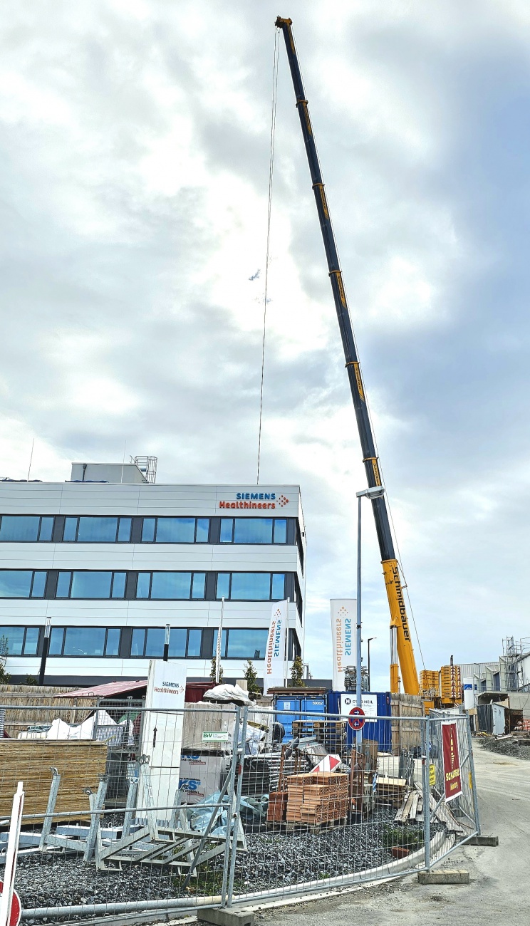 Schwerer Mobilkran auf der Siemens-Baustelle in Kemnath

Ein imposanter Mobilkran der Firma Schmidbauer prägt derzeit das Bild auf der Baustelle von Siemens Healthineers in Kemnath. Mit seinem weit ausgefahrenen Teleskopausleger überragt der Kran das bestehende Firmengebäude deutlich.

Am Standort investiert Siemens Healthineers rund 70 Millionen Euro in eine neue Montage- und Fertigungshalle. Die Erweiterung soll Mitte 2027 in Betrieb gehen und den Medizintechnikstandort Kemnath weiter stärken.