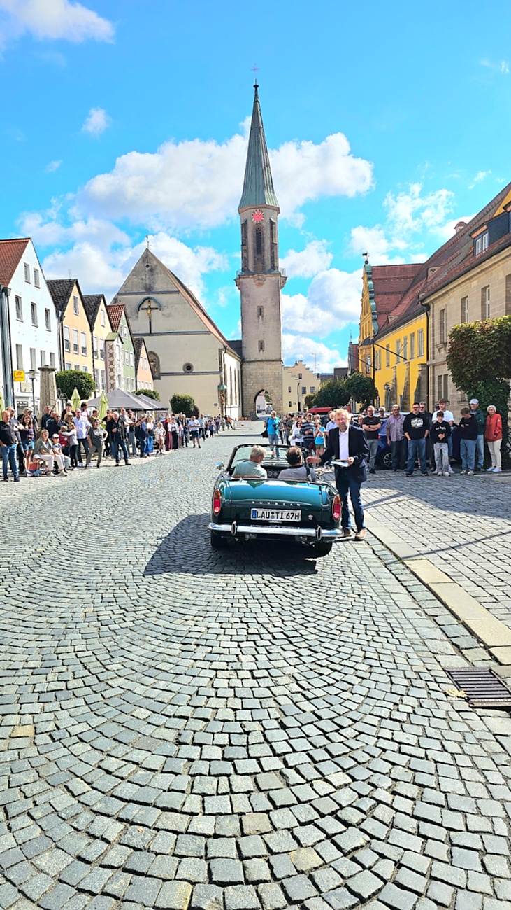 Jede Menge automobile Schätze auf dem Kemnather Stadtplatz

Ein echtes Paradies für Oldtimerfreunde gab es am Samstag beim großen Oldtimertreffen in Kemnath zu erleben. Ab 10 Uhr gehörte der wunderschöne historische Stadtplatz den automobilen Schätzen vergangener Jahrzehnte. Bei bestem Oldtimerwetter präsentierten sich die liebevoll gepflegten Fahrzeuge vor einer traumhaften Kulisse – und natürlich ließen sich das auch jede Menge Zuschauer nicht entgehen.

Dicht an dicht standen die Besucher entlang des Stadtplatzes, als ein Klassiker nach dem anderen zur Fahrzeugvorstellung vorfuhr. Dabei gab es nicht nur jede Menge Chrom, glänzenden Lack und den unverwechselbaren Klang alter Motoren zu bestaunen, sondern auch viel Wissenswertes zu hören.

Wie jedes Jahr hatte Elmar Högl das Mikrofon fest im Griff. Souverän und mit enormem Fachwissen stellte er die einzelnen Fahrzeuge vor, erzählte von Baujahren, Motorisierung und technischen Besonderheiten und hatte dabei immer wieder interessante Details zu den Oldtimern parat.

Und eigentlich ist Elmar Högl aus dem Kemnather Oldtimertreffen kaum wegzudenken. Er ist nicht nur die bekannte Stimme am Mikrofon, sondern zugleich Hauptorganisator und so etwas wie das „Herz“ des Treffens. Gemeinsam mit dem KEM-Verband und der Stadt Kemnath sorgt er dafür, dass die Freunde historischer Fahrzeuge Jahr für Jahr in Kemnath zusammenkommen.

Zur Fahrzeugvorstellung gehörte natürlich auch die Übergabe der Urkunden. Diese Aufgabe übernahm Hermann Schraml, unterstützt von Stefan Wöhrl.

Und besser hätte es an diesem Vormittag eigentlich kaum passen können: herrliches Wetter, ein voller Stadtplatz, viele begeisterte Zuschauer und mittendrin jede Menge automobile Zeitgeschichte auf zwei und vier Rädern.

Nach der Vorstellung blieb noch genügend Zeit, die Oldtimer aus nächster Nähe zu betrachten, mit den Besitzern ins Gespräch zu kommen und natürlich jede Menge Fotos zu machen.

Am Nachmittag wartete dann bereits der nächste Höhepunkt auf die Teilnehmer. Um 13:15 Uhr machten sich die historischen Fahrzeuge zur gemeinsamen Ausfahrt auf den Weg. Über Berndorf, Haidenaab und Weidenberg führte die Tour unter anderem nach Goldkronach, wo eine längere Rast eingelegt wurde, bevor es schließlich wieder zurück nach Kemnath ging.

Und jetzt viel Spaß beim Durchklicken durch unsere Bilder vom Kemnather Oldtimertreffen 2026!