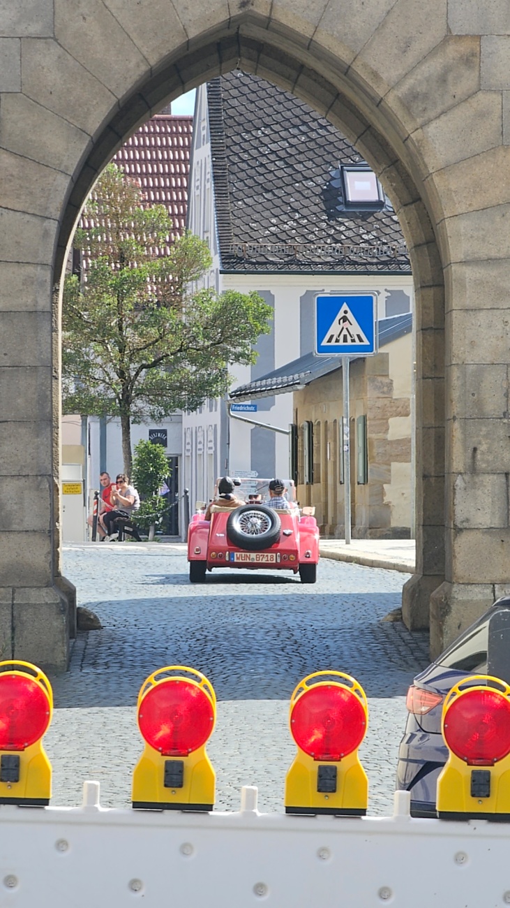 Jede Menge automobile Schätze auf dem Kemnather Stadtplatz

Ein echtes Paradies für Oldtimerfreunde gab es am Samstag beim großen Oldtimertreffen in Kemnath zu erleben. Ab 10 Uhr gehörte der wunderschöne historische Stadtplatz den automobilen Schätzen vergangener Jahrzehnte. Bei bestem Oldtimerwetter präsentierten sich die liebevoll gepflegten Fahrzeuge vor einer traumhaften Kulisse – und natürlich ließen sich das auch jede Menge Zuschauer nicht entgehen.

Dicht an dicht standen die Besucher entlang des Stadtplatzes, als ein Klassiker nach dem anderen zur Fahrzeugvorstellung vorfuhr. Dabei gab es nicht nur jede Menge Chrom, glänzenden Lack und den unverwechselbaren Klang alter Motoren zu bestaunen, sondern auch viel Wissenswertes zu hören.

Wie jedes Jahr hatte Elmar Högl das Mikrofon fest im Griff. Souverän und mit enormem Fachwissen stellte er die einzelnen Fahrzeuge vor, erzählte von Baujahren, Motorisierung und technischen Besonderheiten und hatte dabei immer wieder interessante Details zu den Oldtimern parat.

Und eigentlich ist Elmar Högl aus dem Kemnather Oldtimertreffen kaum wegzudenken. Er ist nicht nur die bekannte Stimme am Mikrofon, sondern zugleich Hauptorganisator und so etwas wie das „Herz“ des Treffens. Gemeinsam mit dem KEM-Verband und der Stadt Kemnath sorgt er dafür, dass die Freunde historischer Fahrzeuge Jahr für Jahr in Kemnath zusammenkommen.

Zur Fahrzeugvorstellung gehörte natürlich auch die Übergabe der Urkunden. Diese Aufgabe übernahm Hermann Schraml, unterstützt von Stefan Wöhrl.

Und besser hätte es an diesem Vormittag eigentlich kaum passen können: herrliches Wetter, ein voller Stadtplatz, viele begeisterte Zuschauer und mittendrin jede Menge automobile Zeitgeschichte auf zwei und vier Rädern.

Nach der Vorstellung blieb noch genügend Zeit, die Oldtimer aus nächster Nähe zu betrachten, mit den Besitzern ins Gespräch zu kommen und natürlich jede Menge Fotos zu machen.

Am Nachmittag wartete dann bereits der nächste Höhepunkt auf die Teilnehmer. Um 13:15 Uhr machten sich die historischen Fahrzeuge zur gemeinsamen Ausfahrt auf den Weg. Über Berndorf, Haidenaab und Weidenberg führte die Tour unter anderem nach Goldkronach, wo eine längere Rast eingelegt wurde, bevor es schließlich wieder zurück nach Kemnath ging.

Und jetzt viel Spaß beim Durchklicken durch unsere Bilder vom Kemnather Oldtimertreffen 2026!