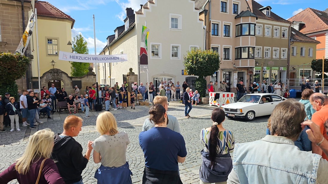 Jede Menge automobile Schätze auf dem Kemnather Stadtplatz

Ein echtes Paradies für Oldtimerfreunde gab es am Samstag beim großen Oldtimertreffen in Kemnath zu erleben. Ab 10 Uhr gehörte der wunderschöne historische Stadtplatz den automobilen Schätzen vergangener Jahrzehnte. Bei bestem Oldtimerwetter präsentierten sich die liebevoll gepflegten Fahrzeuge vor einer traumhaften Kulisse – und natürlich ließen sich das auch jede Menge Zuschauer nicht entgehen.

Dicht an dicht standen die Besucher entlang des Stadtplatzes, als ein Klassiker nach dem anderen zur Fahrzeugvorstellung vorfuhr. Dabei gab es nicht nur jede Menge Chrom, glänzenden Lack und den unverwechselbaren Klang alter Motoren zu bestaunen, sondern auch viel Wissenswertes zu hören.

Wie jedes Jahr hatte Elmar Högl das Mikrofon fest im Griff. Souverän und mit enormem Fachwissen stellte er die einzelnen Fahrzeuge vor, erzählte von Baujahren, Motorisierung und technischen Besonderheiten und hatte dabei immer wieder interessante Details zu den Oldtimern parat.

Und eigentlich ist Elmar Högl aus dem Kemnather Oldtimertreffen kaum wegzudenken. Er ist nicht nur die bekannte Stimme am Mikrofon, sondern zugleich Hauptorganisator und so etwas wie das „Herz“ des Treffens. Gemeinsam mit dem KEM-Verband und der Stadt Kemnath sorgt er dafür, dass die Freunde historischer Fahrzeuge Jahr für Jahr in Kemnath zusammenkommen.

Zur Fahrzeugvorstellung gehörte natürlich auch die Übergabe der Urkunden. Diese Aufgabe übernahm Hermann Schraml, unterstützt von Stefan Wöhrl.

Und besser hätte es an diesem Vormittag eigentlich kaum passen können: herrliches Wetter, ein voller Stadtplatz, viele begeisterte Zuschauer und mittendrin jede Menge automobile Zeitgeschichte auf zwei und vier Rädern.

Nach der Vorstellung blieb noch genügend Zeit, die Oldtimer aus nächster Nähe zu betrachten, mit den Besitzern ins Gespräch zu kommen und natürlich jede Menge Fotos zu machen.

Am Nachmittag wartete dann bereits der nächste Höhepunkt auf die Teilnehmer. Um 13:15 Uhr machten sich die historischen Fahrzeuge zur gemeinsamen Ausfahrt auf den Weg. Über Berndorf, Haidenaab und Weidenberg führte die Tour unter anderem nach Goldkronach, wo eine längere Rast eingelegt wurde, bevor es schließlich wieder zurück nach Kemnath ging.

Und jetzt viel Spaß beim Durchklicken durch unsere Bilder vom Kemnather Oldtimertreffen 2026!