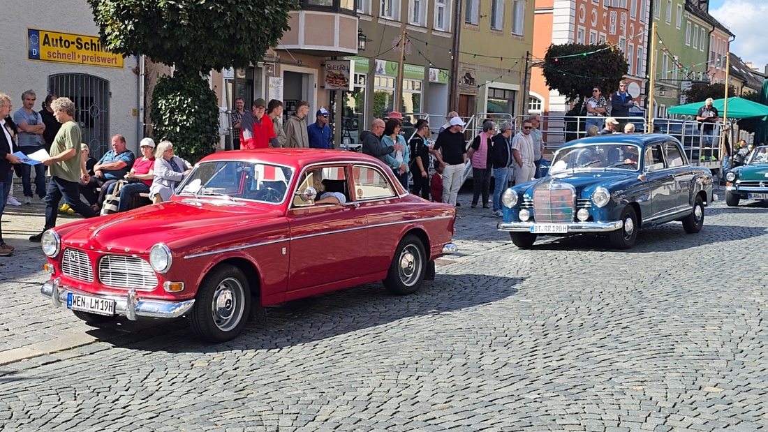 Jede Menge automobile Schätze auf dem Kemnather Stadtplatz

Ein echtes Paradies für Oldtimerfreunde gab es am Samstag beim großen Oldtimertreffen in Kemnath zu erleben. Ab 10 Uhr gehörte der wunderschöne historische Stadtplatz den automobilen Schätzen vergangener Jahrzehnte. Bei bestem Oldtimerwetter präsentierten sich die liebevoll gepflegten Fahrzeuge vor einer traumhaften Kulisse – und natürlich ließen sich das auch jede Menge Zuschauer nicht entgehen.

Dicht an dicht standen die Besucher entlang des Stadtplatzes, als ein Klassiker nach dem anderen zur Fahrzeugvorstellung vorfuhr. Dabei gab es nicht nur jede Menge Chrom, glänzenden Lack und den unverwechselbaren Klang alter Motoren zu bestaunen, sondern auch viel Wissenswertes zu hören.

Wie jedes Jahr hatte Elmar Högl das Mikrofon fest im Griff. Souverän und mit enormem Fachwissen stellte er die einzelnen Fahrzeuge vor, erzählte von Baujahren, Motorisierung und technischen Besonderheiten und hatte dabei immer wieder interessante Details zu den Oldtimern parat.

Und eigentlich ist Elmar Högl aus dem Kemnather Oldtimertreffen kaum wegzudenken. Er ist nicht nur die bekannte Stimme am Mikrofon, sondern zugleich Hauptorganisator und so etwas wie das „Herz“ des Treffens. Gemeinsam mit dem KEM-Verband und der Stadt Kemnath sorgt er dafür, dass die Freunde historischer Fahrzeuge Jahr für Jahr in Kemnath zusammenkommen.

Zur Fahrzeugvorstellung gehörte natürlich auch die Übergabe der Urkunden. Diese Aufgabe übernahm Hermann Schraml, unterstützt von Stefan Wöhrl.

Und besser hätte es an diesem Vormittag eigentlich kaum passen können: herrliches Wetter, ein voller Stadtplatz, viele begeisterte Zuschauer und mittendrin jede Menge automobile Zeitgeschichte auf zwei und vier Rädern.

Nach der Vorstellung blieb noch genügend Zeit, die Oldtimer aus nächster Nähe zu betrachten, mit den Besitzern ins Gespräch zu kommen und natürlich jede Menge Fotos zu machen.

Am Nachmittag wartete dann bereits der nächste Höhepunkt auf die Teilnehmer. Um 13:15 Uhr machten sich die historischen Fahrzeuge zur gemeinsamen Ausfahrt auf den Weg. Über Berndorf, Haidenaab und Weidenberg führte die Tour unter anderem nach Goldkronach, wo eine längere Rast eingelegt wurde, bevor es schließlich wieder zurück nach Kemnath ging.

Und jetzt viel Spaß beim Durchklicken durch unsere Bilder vom Kemnather Oldtimertreffen 2026!