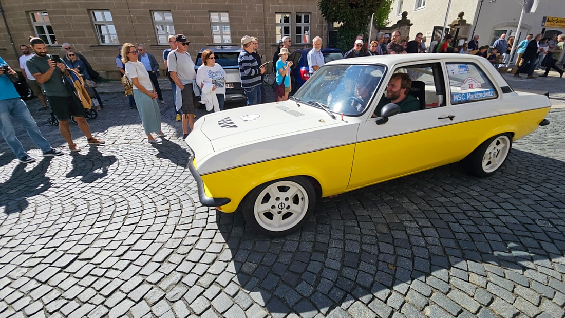 Jede Menge automobile Schätze auf dem Kemnather Stadtplatz

Ein echtes Paradies für Oldtimerfreunde gab es am Samstag beim großen Oldtimertreffen in Kemnath zu erleben. Ab 10 Uhr gehörte der wunderschöne historische Stadtplatz den automobilen Schätzen vergangener Jahrzehnte. Bei bestem Oldtimerwetter präsentierten sich die liebevoll gepflegten Fahrzeuge vor einer traumhaften Kulisse – und natürlich ließen sich das auch jede Menge Zuschauer nicht entgehen.

Dicht an dicht standen die Besucher entlang des Stadtplatzes, als ein Klassiker nach dem anderen zur Fahrzeugvorstellung vorfuhr. Dabei gab es nicht nur jede Menge Chrom, glänzenden Lack und den unverwechselbaren Klang alter Motoren zu bestaunen, sondern auch viel Wissenswertes zu hören.

Wie jedes Jahr hatte Elmar Högl das Mikrofon fest im Griff. Souverän und mit enormem Fachwissen stellte er die einzelnen Fahrzeuge vor, erzählte von Baujahren, Motorisierung und technischen Besonderheiten und hatte dabei immer wieder interessante Details zu den Oldtimern parat.

Und eigentlich ist Elmar Högl aus dem Kemnather Oldtimertreffen kaum wegzudenken. Er ist nicht nur die bekannte Stimme am Mikrofon, sondern zugleich Hauptorganisator und so etwas wie das „Herz“ des Treffens. Gemeinsam mit dem KEM-Verband und der Stadt Kemnath sorgt er dafür, dass die Freunde historischer Fahrzeuge Jahr für Jahr in Kemnath zusammenkommen.

Zur Fahrzeugvorstellung gehörte natürlich auch die Übergabe der Urkunden. Diese Aufgabe übernahm Hermann Schraml, unterstützt von Stefan Wöhrl.

Und besser hätte es an diesem Vormittag eigentlich kaum passen können: herrliches Wetter, ein voller Stadtplatz, viele begeisterte Zuschauer und mittendrin jede Menge automobile Zeitgeschichte auf zwei und vier Rädern.

Nach der Vorstellung blieb noch genügend Zeit, die Oldtimer aus nächster Nähe zu betrachten, mit den Besitzern ins Gespräch zu kommen und natürlich jede Menge Fotos zu machen.

Am Nachmittag wartete dann bereits der nächste Höhepunkt auf die Teilnehmer. Um 13:15 Uhr machten sich die historischen Fahrzeuge zur gemeinsamen Ausfahrt auf den Weg. Über Berndorf, Haidenaab und Weidenberg führte die Tour unter anderem nach Goldkronach, wo eine längere Rast eingelegt wurde, bevor es schließlich wieder zurück nach Kemnath ging.

Und jetzt viel Spaß beim Durchklicken durch unsere Bilder vom Kemnather Oldtimertreffen 2026!