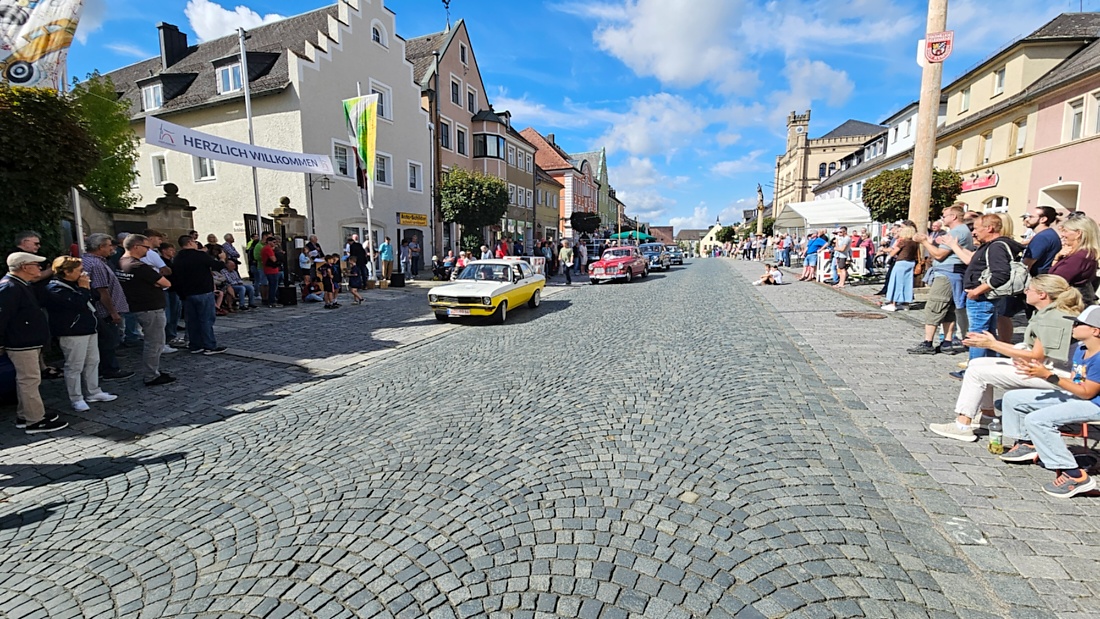 Jede Menge automobile Schätze auf dem Kemnather Stadtplatz

Ein echtes Paradies für Oldtimerfreunde gab es am Samstag beim großen Oldtimertreffen in Kemnath zu erleben. Ab 10 Uhr gehörte der wunderschöne historische Stadtplatz den automobilen Schätzen vergangener Jahrzehnte. Bei bestem Oldtimerwetter präsentierten sich die liebevoll gepflegten Fahrzeuge vor einer traumhaften Kulisse – und natürlich ließen sich das auch jede Menge Zuschauer nicht entgehen.

Dicht an dicht standen die Besucher entlang des Stadtplatzes, als ein Klassiker nach dem anderen zur Fahrzeugvorstellung vorfuhr. Dabei gab es nicht nur jede Menge Chrom, glänzenden Lack und den unverwechselbaren Klang alter Motoren zu bestaunen, sondern auch viel Wissenswertes zu hören.

Wie jedes Jahr hatte Elmar Högl das Mikrofon fest im Griff. Souverän und mit enormem Fachwissen stellte er die einzelnen Fahrzeuge vor, erzählte von Baujahren, Motorisierung und technischen Besonderheiten und hatte dabei immer wieder interessante Details zu den Oldtimern parat.

Und eigentlich ist Elmar Högl aus dem Kemnather Oldtimertreffen kaum wegzudenken. Er ist nicht nur die bekannte Stimme am Mikrofon, sondern zugleich Hauptorganisator und so etwas wie das „Herz“ des Treffens. Gemeinsam mit dem KEM-Verband und der Stadt Kemnath sorgt er dafür, dass die Freunde historischer Fahrzeuge Jahr für Jahr in Kemnath zusammenkommen.

Zur Fahrzeugvorstellung gehörte natürlich auch die Übergabe der Urkunden. Diese Aufgabe übernahm Hermann Schraml, unterstützt von Stefan Wöhrl.

Und besser hätte es an diesem Vormittag eigentlich kaum passen können: herrliches Wetter, ein voller Stadtplatz, viele begeisterte Zuschauer und mittendrin jede Menge automobile Zeitgeschichte auf zwei und vier Rädern.

Nach der Vorstellung blieb noch genügend Zeit, die Oldtimer aus nächster Nähe zu betrachten, mit den Besitzern ins Gespräch zu kommen und natürlich jede Menge Fotos zu machen.

Am Nachmittag wartete dann bereits der nächste Höhepunkt auf die Teilnehmer. Um 13:15 Uhr machten sich die historischen Fahrzeuge zur gemeinsamen Ausfahrt auf den Weg. Über Berndorf, Haidenaab und Weidenberg führte die Tour unter anderem nach Goldkronach, wo eine längere Rast eingelegt wurde, bevor es schließlich wieder zurück nach Kemnath ging.

Und jetzt viel Spaß beim Durchklicken durch unsere Bilder vom Kemnather Oldtimertreffen 2026!