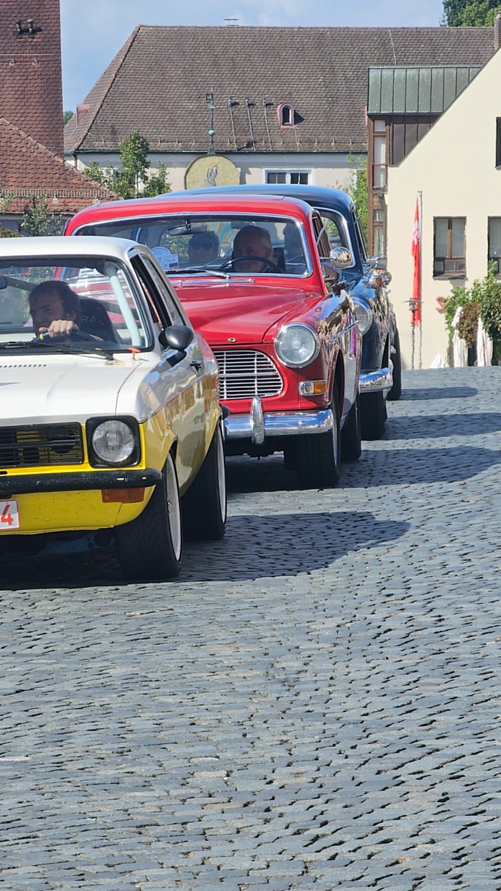 Jede Menge automobile Schätze auf dem Kemnather Stadtplatz

Ein echtes Paradies für Oldtimerfreunde gab es am Samstag beim großen Oldtimertreffen in Kemnath zu erleben. Ab 10 Uhr gehörte der wunderschöne historische Stadtplatz den automobilen Schätzen vergangener Jahrzehnte. Bei bestem Oldtimerwetter präsentierten sich die liebevoll gepflegten Fahrzeuge vor einer traumhaften Kulisse – und natürlich ließen sich das auch jede Menge Zuschauer nicht entgehen.

Dicht an dicht standen die Besucher entlang des Stadtplatzes, als ein Klassiker nach dem anderen zur Fahrzeugvorstellung vorfuhr. Dabei gab es nicht nur jede Menge Chrom, glänzenden Lack und den unverwechselbaren Klang alter Motoren zu bestaunen, sondern auch viel Wissenswertes zu hören.

Wie jedes Jahr hatte Elmar Högl das Mikrofon fest im Griff. Souverän und mit enormem Fachwissen stellte er die einzelnen Fahrzeuge vor, erzählte von Baujahren, Motorisierung und technischen Besonderheiten und hatte dabei immer wieder interessante Details zu den Oldtimern parat.

Und eigentlich ist Elmar Högl aus dem Kemnather Oldtimertreffen kaum wegzudenken. Er ist nicht nur die bekannte Stimme am Mikrofon, sondern zugleich Hauptorganisator und so etwas wie das „Herz“ des Treffens. Gemeinsam mit dem KEM-Verband und der Stadt Kemnath sorgt er dafür, dass die Freunde historischer Fahrzeuge Jahr für Jahr in Kemnath zusammenkommen.

Zur Fahrzeugvorstellung gehörte natürlich auch die Übergabe der Urkunden. Diese Aufgabe übernahm Hermann Schraml, unterstützt von Stefan Wöhrl.

Und besser hätte es an diesem Vormittag eigentlich kaum passen können: herrliches Wetter, ein voller Stadtplatz, viele begeisterte Zuschauer und mittendrin jede Menge automobile Zeitgeschichte auf zwei und vier Rädern.

Nach der Vorstellung blieb noch genügend Zeit, die Oldtimer aus nächster Nähe zu betrachten, mit den Besitzern ins Gespräch zu kommen und natürlich jede Menge Fotos zu machen.

Am Nachmittag wartete dann bereits der nächste Höhepunkt auf die Teilnehmer. Um 13:15 Uhr machten sich die historischen Fahrzeuge zur gemeinsamen Ausfahrt auf den Weg. Über Berndorf, Haidenaab und Weidenberg führte die Tour unter anderem nach Goldkronach, wo eine längere Rast eingelegt wurde, bevor es schließlich wieder zurück nach Kemnath ging.

Und jetzt viel Spaß beim Durchklicken durch unsere Bilder vom Kemnather Oldtimertreffen 2026!