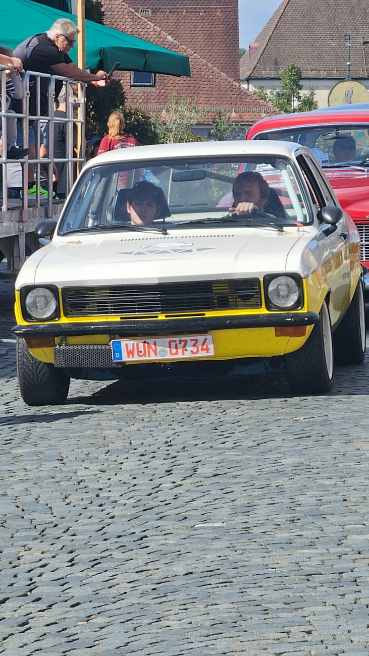 Jede Menge automobile Schätze auf dem Kemnather Stadtplatz

Ein echtes Paradies für Oldtimerfreunde gab es am Samstag beim großen Oldtimertreffen in Kemnath zu erleben. Ab 10 Uhr gehörte der wunderschöne historische Stadtplatz den automobilen Schätzen vergangener Jahrzehnte. Bei bestem Oldtimerwetter präsentierten sich die liebevoll gepflegten Fahrzeuge vor einer traumhaften Kulisse – und natürlich ließen sich das auch jede Menge Zuschauer nicht entgehen.

Dicht an dicht standen die Besucher entlang des Stadtplatzes, als ein Klassiker nach dem anderen zur Fahrzeugvorstellung vorfuhr. Dabei gab es nicht nur jede Menge Chrom, glänzenden Lack und den unverwechselbaren Klang alter Motoren zu bestaunen, sondern auch viel Wissenswertes zu hören.

Wie jedes Jahr hatte Elmar Högl das Mikrofon fest im Griff. Souverän und mit enormem Fachwissen stellte er die einzelnen Fahrzeuge vor, erzählte von Baujahren, Motorisierung und technischen Besonderheiten und hatte dabei immer wieder interessante Details zu den Oldtimern parat.

Und eigentlich ist Elmar Högl aus dem Kemnather Oldtimertreffen kaum wegzudenken. Er ist nicht nur die bekannte Stimme am Mikrofon, sondern zugleich Hauptorganisator und so etwas wie das „Herz“ des Treffens. Gemeinsam mit dem KEM-Verband und der Stadt Kemnath sorgt er dafür, dass die Freunde historischer Fahrzeuge Jahr für Jahr in Kemnath zusammenkommen.

Zur Fahrzeugvorstellung gehörte natürlich auch die Übergabe der Urkunden. Diese Aufgabe übernahm Hermann Schraml, unterstützt von Stefan Wöhrl.

Und besser hätte es an diesem Vormittag eigentlich kaum passen können: herrliches Wetter, ein voller Stadtplatz, viele begeisterte Zuschauer und mittendrin jede Menge automobile Zeitgeschichte auf zwei und vier Rädern.

Nach der Vorstellung blieb noch genügend Zeit, die Oldtimer aus nächster Nähe zu betrachten, mit den Besitzern ins Gespräch zu kommen und natürlich jede Menge Fotos zu machen.

Am Nachmittag wartete dann bereits der nächste Höhepunkt auf die Teilnehmer. Um 13:15 Uhr machten sich die historischen Fahrzeuge zur gemeinsamen Ausfahrt auf den Weg. Über Berndorf, Haidenaab und Weidenberg führte die Tour unter anderem nach Goldkronach, wo eine längere Rast eingelegt wurde, bevor es schließlich wieder zurück nach Kemnath ging.

Und jetzt viel Spaß beim Durchklicken durch unsere Bilder vom Kemnather Oldtimertreffen 2026!