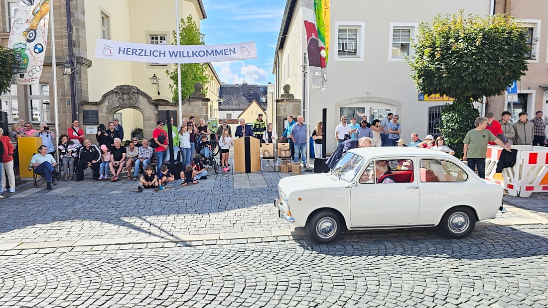 Jede Menge automobile Schätze auf dem Kemnather Stadtplatz

Ein echtes Paradies für Oldtimerfreunde gab es am Samstag beim großen Oldtimertreffen in Kemnath zu erleben. Ab 10 Uhr gehörte der wunderschöne historische Stadtplatz den automobilen Schätzen vergangener Jahrzehnte. Bei bestem Oldtimerwetter präsentierten sich die liebevoll gepflegten Fahrzeuge vor einer traumhaften Kulisse – und natürlich ließen sich das auch jede Menge Zuschauer nicht entgehen.

Dicht an dicht standen die Besucher entlang des Stadtplatzes, als ein Klassiker nach dem anderen zur Fahrzeugvorstellung vorfuhr. Dabei gab es nicht nur jede Menge Chrom, glänzenden Lack und den unverwechselbaren Klang alter Motoren zu bestaunen, sondern auch viel Wissenswertes zu hören.

Wie jedes Jahr hatte Elmar Högl das Mikrofon fest im Griff. Souverän und mit enormem Fachwissen stellte er die einzelnen Fahrzeuge vor, erzählte von Baujahren, Motorisierung und technischen Besonderheiten und hatte dabei immer wieder interessante Details zu den Oldtimern parat.

Und eigentlich ist Elmar Högl aus dem Kemnather Oldtimertreffen kaum wegzudenken. Er ist nicht nur die bekannte Stimme am Mikrofon, sondern zugleich Hauptorganisator und so etwas wie das „Herz“ des Treffens. Gemeinsam mit dem KEM-Verband und der Stadt Kemnath sorgt er dafür, dass die Freunde historischer Fahrzeuge Jahr für Jahr in Kemnath zusammenkommen.

Zur Fahrzeugvorstellung gehörte natürlich auch die Übergabe der Urkunden. Diese Aufgabe übernahm Hermann Schraml, unterstützt von Stefan Wöhrl.

Und besser hätte es an diesem Vormittag eigentlich kaum passen können: herrliches Wetter, ein voller Stadtplatz, viele begeisterte Zuschauer und mittendrin jede Menge automobile Zeitgeschichte auf zwei und vier Rädern.

Nach der Vorstellung blieb noch genügend Zeit, die Oldtimer aus nächster Nähe zu betrachten, mit den Besitzern ins Gespräch zu kommen und natürlich jede Menge Fotos zu machen.

Am Nachmittag wartete dann bereits der nächste Höhepunkt auf die Teilnehmer. Um 13:15 Uhr machten sich die historischen Fahrzeuge zur gemeinsamen Ausfahrt auf den Weg. Über Berndorf, Haidenaab und Weidenberg führte die Tour unter anderem nach Goldkronach, wo eine längere Rast eingelegt wurde, bevor es schließlich wieder zurück nach Kemnath ging.

Und jetzt viel Spaß beim Durchklicken durch unsere Bilder vom Kemnather Oldtimertreffen 2026!