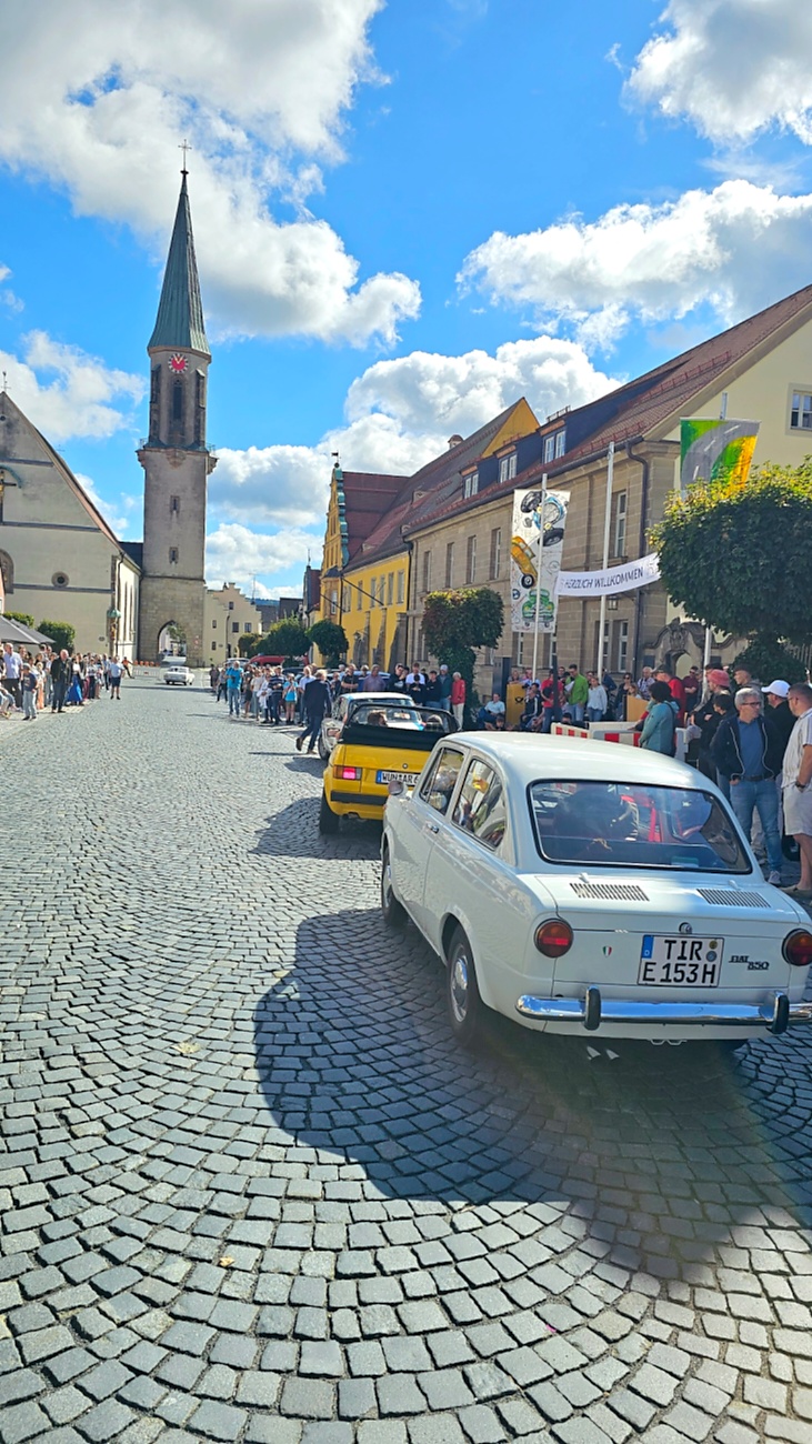 Jede Menge automobile Schätze auf dem Kemnather Stadtplatz

Ein echtes Paradies für Oldtimerfreunde gab es am Samstag beim großen Oldtimertreffen in Kemnath zu erleben. Ab 10 Uhr gehörte der wunderschöne historische Stadtplatz den automobilen Schätzen vergangener Jahrzehnte. Bei bestem Oldtimerwetter präsentierten sich die liebevoll gepflegten Fahrzeuge vor einer traumhaften Kulisse – und natürlich ließen sich das auch jede Menge Zuschauer nicht entgehen.

Dicht an dicht standen die Besucher entlang des Stadtplatzes, als ein Klassiker nach dem anderen zur Fahrzeugvorstellung vorfuhr. Dabei gab es nicht nur jede Menge Chrom, glänzenden Lack und den unverwechselbaren Klang alter Motoren zu bestaunen, sondern auch viel Wissenswertes zu hören.

Wie jedes Jahr hatte Elmar Högl das Mikrofon fest im Griff. Souverän und mit enormem Fachwissen stellte er die einzelnen Fahrzeuge vor, erzählte von Baujahren, Motorisierung und technischen Besonderheiten und hatte dabei immer wieder interessante Details zu den Oldtimern parat.

Und eigentlich ist Elmar Högl aus dem Kemnather Oldtimertreffen kaum wegzudenken. Er ist nicht nur die bekannte Stimme am Mikrofon, sondern zugleich Hauptorganisator und so etwas wie das „Herz“ des Treffens. Gemeinsam mit dem KEM-Verband und der Stadt Kemnath sorgt er dafür, dass die Freunde historischer Fahrzeuge Jahr für Jahr in Kemnath zusammenkommen.

Zur Fahrzeugvorstellung gehörte natürlich auch die Übergabe der Urkunden. Diese Aufgabe übernahm Hermann Schraml, unterstützt von Stefan Wöhrl.

Und besser hätte es an diesem Vormittag eigentlich kaum passen können: herrliches Wetter, ein voller Stadtplatz, viele begeisterte Zuschauer und mittendrin jede Menge automobile Zeitgeschichte auf zwei und vier Rädern.

Nach der Vorstellung blieb noch genügend Zeit, die Oldtimer aus nächster Nähe zu betrachten, mit den Besitzern ins Gespräch zu kommen und natürlich jede Menge Fotos zu machen.

Am Nachmittag wartete dann bereits der nächste Höhepunkt auf die Teilnehmer. Um 13:15 Uhr machten sich die historischen Fahrzeuge zur gemeinsamen Ausfahrt auf den Weg. Über Berndorf, Haidenaab und Weidenberg führte die Tour unter anderem nach Goldkronach, wo eine längere Rast eingelegt wurde, bevor es schließlich wieder zurück nach Kemnath ging.

Und jetzt viel Spaß beim Durchklicken durch unsere Bilder vom Kemnather Oldtimertreffen 2026!