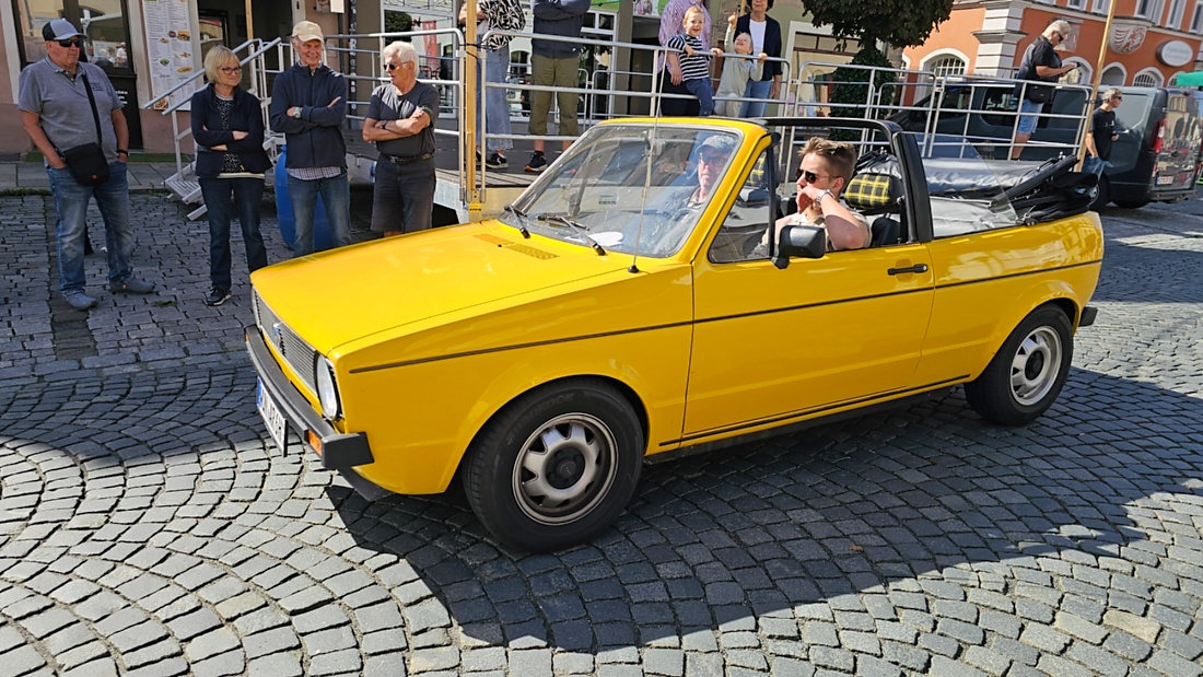 Jede Menge automobile Schätze auf dem Kemnather Stadtplatz

Ein echtes Paradies für Oldtimerfreunde gab es am Samstag beim großen Oldtimertreffen in Kemnath zu erleben. Ab 10 Uhr gehörte der wunderschöne historische Stadtplatz den automobilen Schätzen vergangener Jahrzehnte. Bei bestem Oldtimerwetter präsentierten sich die liebevoll gepflegten Fahrzeuge vor einer traumhaften Kulisse – und natürlich ließen sich das auch jede Menge Zuschauer nicht entgehen.

Dicht an dicht standen die Besucher entlang des Stadtplatzes, als ein Klassiker nach dem anderen zur Fahrzeugvorstellung vorfuhr. Dabei gab es nicht nur jede Menge Chrom, glänzenden Lack und den unverwechselbaren Klang alter Motoren zu bestaunen, sondern auch viel Wissenswertes zu hören.

Wie jedes Jahr hatte Elmar Högl das Mikrofon fest im Griff. Souverän und mit enormem Fachwissen stellte er die einzelnen Fahrzeuge vor, erzählte von Baujahren, Motorisierung und technischen Besonderheiten und hatte dabei immer wieder interessante Details zu den Oldtimern parat.

Und eigentlich ist Elmar Högl aus dem Kemnather Oldtimertreffen kaum wegzudenken. Er ist nicht nur die bekannte Stimme am Mikrofon, sondern zugleich Hauptorganisator und so etwas wie das „Herz“ des Treffens. Gemeinsam mit dem KEM-Verband und der Stadt Kemnath sorgt er dafür, dass die Freunde historischer Fahrzeuge Jahr für Jahr in Kemnath zusammenkommen.

Zur Fahrzeugvorstellung gehörte natürlich auch die Übergabe der Urkunden. Diese Aufgabe übernahm Hermann Schraml, unterstützt von Stefan Wöhrl.

Und besser hätte es an diesem Vormittag eigentlich kaum passen können: herrliches Wetter, ein voller Stadtplatz, viele begeisterte Zuschauer und mittendrin jede Menge automobile Zeitgeschichte auf zwei und vier Rädern.

Nach der Vorstellung blieb noch genügend Zeit, die Oldtimer aus nächster Nähe zu betrachten, mit den Besitzern ins Gespräch zu kommen und natürlich jede Menge Fotos zu machen.

Am Nachmittag wartete dann bereits der nächste Höhepunkt auf die Teilnehmer. Um 13:15 Uhr machten sich die historischen Fahrzeuge zur gemeinsamen Ausfahrt auf den Weg. Über Berndorf, Haidenaab und Weidenberg führte die Tour unter anderem nach Goldkronach, wo eine längere Rast eingelegt wurde, bevor es schließlich wieder zurück nach Kemnath ging.

Und jetzt viel Spaß beim Durchklicken durch unsere Bilder vom Kemnather Oldtimertreffen 2026!