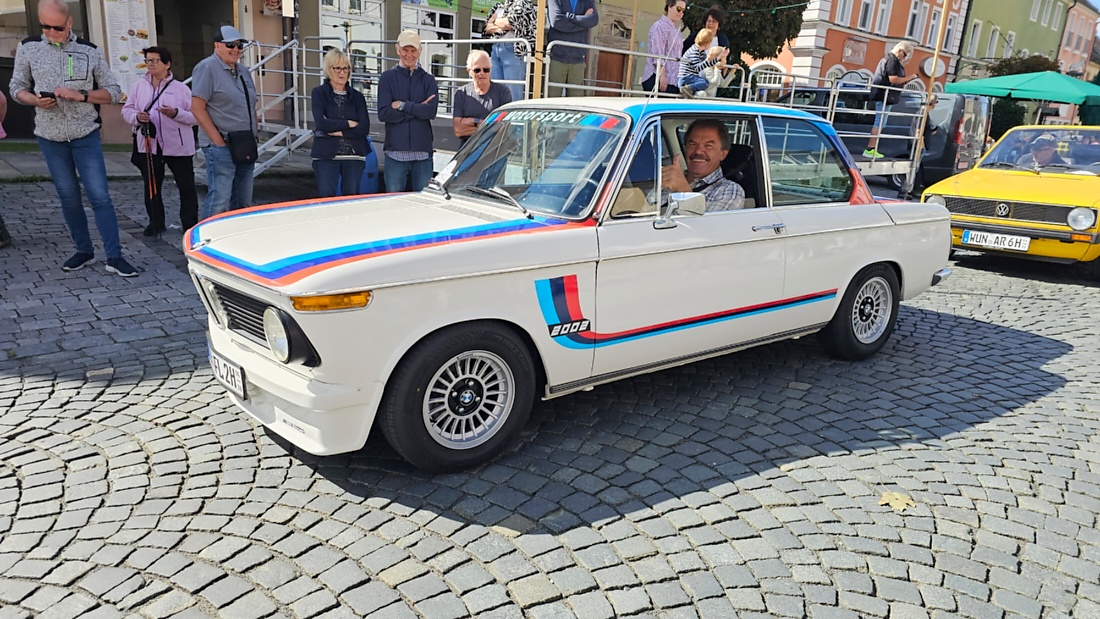 Jede Menge automobile Schätze auf dem Kemnather Stadtplatz

Ein echtes Paradies für Oldtimerfreunde gab es am Samstag beim großen Oldtimertreffen in Kemnath zu erleben. Ab 10 Uhr gehörte der wunderschöne historische Stadtplatz den automobilen Schätzen vergangener Jahrzehnte. Bei bestem Oldtimerwetter präsentierten sich die liebevoll gepflegten Fahrzeuge vor einer traumhaften Kulisse – und natürlich ließen sich das auch jede Menge Zuschauer nicht entgehen.

Dicht an dicht standen die Besucher entlang des Stadtplatzes, als ein Klassiker nach dem anderen zur Fahrzeugvorstellung vorfuhr. Dabei gab es nicht nur jede Menge Chrom, glänzenden Lack und den unverwechselbaren Klang alter Motoren zu bestaunen, sondern auch viel Wissenswertes zu hören.

Wie jedes Jahr hatte Elmar Högl das Mikrofon fest im Griff. Souverän und mit enormem Fachwissen stellte er die einzelnen Fahrzeuge vor, erzählte von Baujahren, Motorisierung und technischen Besonderheiten und hatte dabei immer wieder interessante Details zu den Oldtimern parat.

Und eigentlich ist Elmar Högl aus dem Kemnather Oldtimertreffen kaum wegzudenken. Er ist nicht nur die bekannte Stimme am Mikrofon, sondern zugleich Hauptorganisator und so etwas wie das „Herz“ des Treffens. Gemeinsam mit dem KEM-Verband und der Stadt Kemnath sorgt er dafür, dass die Freunde historischer Fahrzeuge Jahr für Jahr in Kemnath zusammenkommen.

Zur Fahrzeugvorstellung gehörte natürlich auch die Übergabe der Urkunden. Diese Aufgabe übernahm Hermann Schraml, unterstützt von Stefan Wöhrl.

Und besser hätte es an diesem Vormittag eigentlich kaum passen können: herrliches Wetter, ein voller Stadtplatz, viele begeisterte Zuschauer und mittendrin jede Menge automobile Zeitgeschichte auf zwei und vier Rädern.

Nach der Vorstellung blieb noch genügend Zeit, die Oldtimer aus nächster Nähe zu betrachten, mit den Besitzern ins Gespräch zu kommen und natürlich jede Menge Fotos zu machen.

Am Nachmittag wartete dann bereits der nächste Höhepunkt auf die Teilnehmer. Um 13:15 Uhr machten sich die historischen Fahrzeuge zur gemeinsamen Ausfahrt auf den Weg. Über Berndorf, Haidenaab und Weidenberg führte die Tour unter anderem nach Goldkronach, wo eine längere Rast eingelegt wurde, bevor es schließlich wieder zurück nach Kemnath ging.

Und jetzt viel Spaß beim Durchklicken durch unsere Bilder vom Kemnather Oldtimertreffen 2026!
