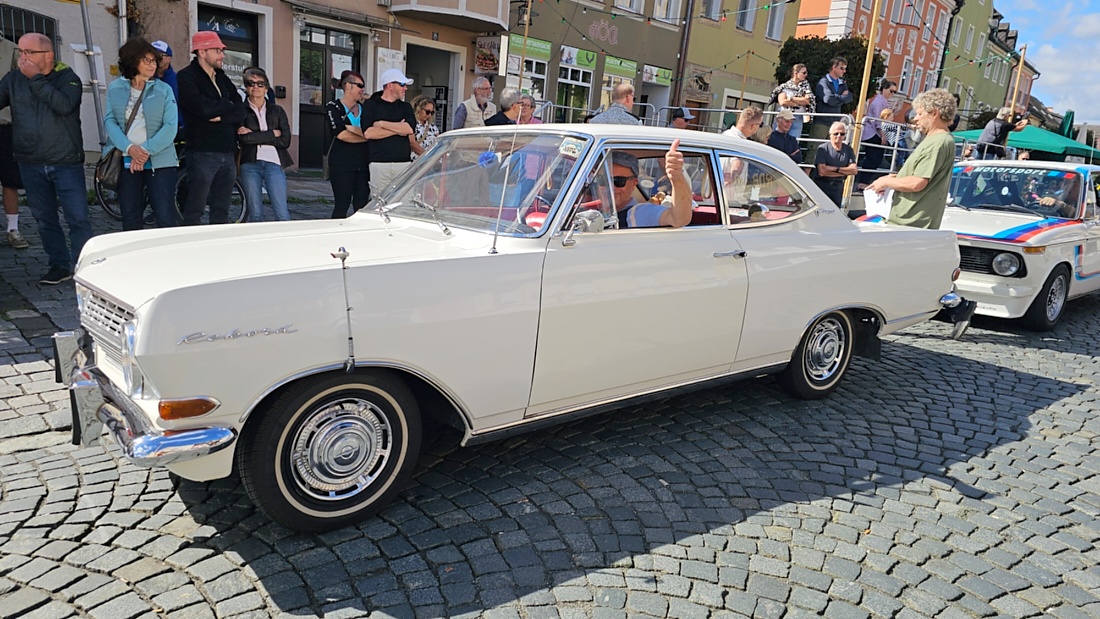 Jede Menge automobile Schätze auf dem Kemnather Stadtplatz

Ein echtes Paradies für Oldtimerfreunde gab es am Samstag beim großen Oldtimertreffen in Kemnath zu erleben. Ab 10 Uhr gehörte der wunderschöne historische Stadtplatz den automobilen Schätzen vergangener Jahrzehnte. Bei bestem Oldtimerwetter präsentierten sich die liebevoll gepflegten Fahrzeuge vor einer traumhaften Kulisse – und natürlich ließen sich das auch jede Menge Zuschauer nicht entgehen.

Dicht an dicht standen die Besucher entlang des Stadtplatzes, als ein Klassiker nach dem anderen zur Fahrzeugvorstellung vorfuhr. Dabei gab es nicht nur jede Menge Chrom, glänzenden Lack und den unverwechselbaren Klang alter Motoren zu bestaunen, sondern auch viel Wissenswertes zu hören.

Wie jedes Jahr hatte Elmar Högl das Mikrofon fest im Griff. Souverän und mit enormem Fachwissen stellte er die einzelnen Fahrzeuge vor, erzählte von Baujahren, Motorisierung und technischen Besonderheiten und hatte dabei immer wieder interessante Details zu den Oldtimern parat.

Und eigentlich ist Elmar Högl aus dem Kemnather Oldtimertreffen kaum wegzudenken. Er ist nicht nur die bekannte Stimme am Mikrofon, sondern zugleich Hauptorganisator und so etwas wie das „Herz“ des Treffens. Gemeinsam mit dem KEM-Verband und der Stadt Kemnath sorgt er dafür, dass die Freunde historischer Fahrzeuge Jahr für Jahr in Kemnath zusammenkommen.

Zur Fahrzeugvorstellung gehörte natürlich auch die Übergabe der Urkunden. Diese Aufgabe übernahm Hermann Schraml, unterstützt von Stefan Wöhrl.

Und besser hätte es an diesem Vormittag eigentlich kaum passen können: herrliches Wetter, ein voller Stadtplatz, viele begeisterte Zuschauer und mittendrin jede Menge automobile Zeitgeschichte auf zwei und vier Rädern.

Nach der Vorstellung blieb noch genügend Zeit, die Oldtimer aus nächster Nähe zu betrachten, mit den Besitzern ins Gespräch zu kommen und natürlich jede Menge Fotos zu machen.

Am Nachmittag wartete dann bereits der nächste Höhepunkt auf die Teilnehmer. Um 13:15 Uhr machten sich die historischen Fahrzeuge zur gemeinsamen Ausfahrt auf den Weg. Über Berndorf, Haidenaab und Weidenberg führte die Tour unter anderem nach Goldkronach, wo eine längere Rast eingelegt wurde, bevor es schließlich wieder zurück nach Kemnath ging.

Und jetzt viel Spaß beim Durchklicken durch unsere Bilder vom Kemnather Oldtimertreffen 2026!