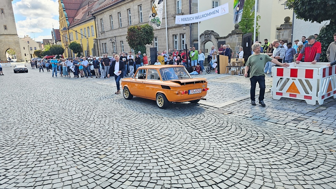 Jede Menge automobile Schätze auf dem Kemnather Stadtplatz

Ein echtes Paradies für Oldtimerfreunde gab es am Samstag beim großen Oldtimertreffen in Kemnath zu erleben. Ab 10 Uhr gehörte der wunderschöne historische Stadtplatz den automobilen Schätzen vergangener Jahrzehnte. Bei bestem Oldtimerwetter präsentierten sich die liebevoll gepflegten Fahrzeuge vor einer traumhaften Kulisse – und natürlich ließen sich das auch jede Menge Zuschauer nicht entgehen.

Dicht an dicht standen die Besucher entlang des Stadtplatzes, als ein Klassiker nach dem anderen zur Fahrzeugvorstellung vorfuhr. Dabei gab es nicht nur jede Menge Chrom, glänzenden Lack und den unverwechselbaren Klang alter Motoren zu bestaunen, sondern auch viel Wissenswertes zu hören.

Wie jedes Jahr hatte Elmar Högl das Mikrofon fest im Griff. Souverän und mit enormem Fachwissen stellte er die einzelnen Fahrzeuge vor, erzählte von Baujahren, Motorisierung und technischen Besonderheiten und hatte dabei immer wieder interessante Details zu den Oldtimern parat.

Und eigentlich ist Elmar Högl aus dem Kemnather Oldtimertreffen kaum wegzudenken. Er ist nicht nur die bekannte Stimme am Mikrofon, sondern zugleich Hauptorganisator und so etwas wie das „Herz“ des Treffens. Gemeinsam mit dem KEM-Verband und der Stadt Kemnath sorgt er dafür, dass die Freunde historischer Fahrzeuge Jahr für Jahr in Kemnath zusammenkommen.

Zur Fahrzeugvorstellung gehörte natürlich auch die Übergabe der Urkunden. Diese Aufgabe übernahm Hermann Schraml, unterstützt von Stefan Wöhrl.

Und besser hätte es an diesem Vormittag eigentlich kaum passen können: herrliches Wetter, ein voller Stadtplatz, viele begeisterte Zuschauer und mittendrin jede Menge automobile Zeitgeschichte auf zwei und vier Rädern.

Nach der Vorstellung blieb noch genügend Zeit, die Oldtimer aus nächster Nähe zu betrachten, mit den Besitzern ins Gespräch zu kommen und natürlich jede Menge Fotos zu machen.

Am Nachmittag wartete dann bereits der nächste Höhepunkt auf die Teilnehmer. Um 13:15 Uhr machten sich die historischen Fahrzeuge zur gemeinsamen Ausfahrt auf den Weg. Über Berndorf, Haidenaab und Weidenberg führte die Tour unter anderem nach Goldkronach, wo eine längere Rast eingelegt wurde, bevor es schließlich wieder zurück nach Kemnath ging.

Und jetzt viel Spaß beim Durchklicken durch unsere Bilder vom Kemnather Oldtimertreffen 2026!