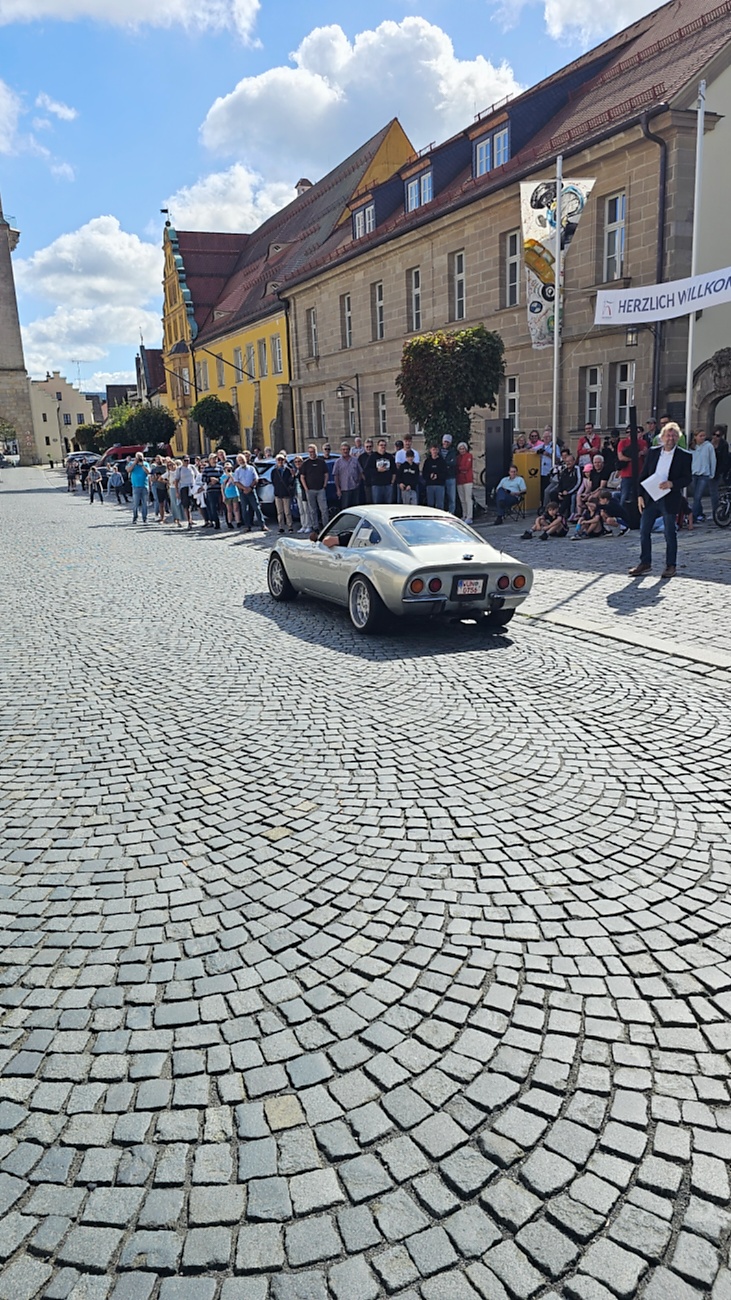 Jede Menge automobile Schätze auf dem Kemnather Stadtplatz

Ein echtes Paradies für Oldtimerfreunde gab es am Samstag beim großen Oldtimertreffen in Kemnath zu erleben. Ab 10 Uhr gehörte der wunderschöne historische Stadtplatz den automobilen Schätzen vergangener Jahrzehnte. Bei bestem Oldtimerwetter präsentierten sich die liebevoll gepflegten Fahrzeuge vor einer traumhaften Kulisse – und natürlich ließen sich das auch jede Menge Zuschauer nicht entgehen.

Dicht an dicht standen die Besucher entlang des Stadtplatzes, als ein Klassiker nach dem anderen zur Fahrzeugvorstellung vorfuhr. Dabei gab es nicht nur jede Menge Chrom, glänzenden Lack und den unverwechselbaren Klang alter Motoren zu bestaunen, sondern auch viel Wissenswertes zu hören.

Wie jedes Jahr hatte Elmar Högl das Mikrofon fest im Griff. Souverän und mit enormem Fachwissen stellte er die einzelnen Fahrzeuge vor, erzählte von Baujahren, Motorisierung und technischen Besonderheiten und hatte dabei immer wieder interessante Details zu den Oldtimern parat.

Und eigentlich ist Elmar Högl aus dem Kemnather Oldtimertreffen kaum wegzudenken. Er ist nicht nur die bekannte Stimme am Mikrofon, sondern zugleich Hauptorganisator und so etwas wie das „Herz“ des Treffens. Gemeinsam mit dem KEM-Verband und der Stadt Kemnath sorgt er dafür, dass die Freunde historischer Fahrzeuge Jahr für Jahr in Kemnath zusammenkommen.

Zur Fahrzeugvorstellung gehörte natürlich auch die Übergabe der Urkunden. Diese Aufgabe übernahm Hermann Schraml, unterstützt von Stefan Wöhrl.

Und besser hätte es an diesem Vormittag eigentlich kaum passen können: herrliches Wetter, ein voller Stadtplatz, viele begeisterte Zuschauer und mittendrin jede Menge automobile Zeitgeschichte auf zwei und vier Rädern.

Nach der Vorstellung blieb noch genügend Zeit, die Oldtimer aus nächster Nähe zu betrachten, mit den Besitzern ins Gespräch zu kommen und natürlich jede Menge Fotos zu machen.

Am Nachmittag wartete dann bereits der nächste Höhepunkt auf die Teilnehmer. Um 13:15 Uhr machten sich die historischen Fahrzeuge zur gemeinsamen Ausfahrt auf den Weg. Über Berndorf, Haidenaab und Weidenberg führte die Tour unter anderem nach Goldkronach, wo eine längere Rast eingelegt wurde, bevor es schließlich wieder zurück nach Kemnath ging.

Und jetzt viel Spaß beim Durchklicken durch unsere Bilder vom Kemnather Oldtimertreffen 2026!