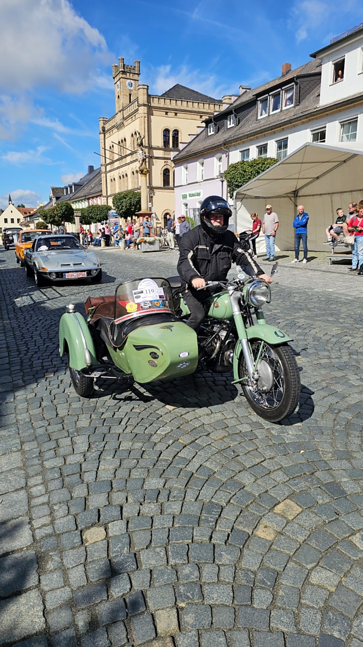 Jede Menge automobile Schätze auf dem Kemnather Stadtplatz

Ein echtes Paradies für Oldtimerfreunde gab es am Samstag beim großen Oldtimertreffen in Kemnath zu erleben. Ab 10 Uhr gehörte der wunderschöne historische Stadtplatz den automobilen Schätzen vergangener Jahrzehnte. Bei bestem Oldtimerwetter präsentierten sich die liebevoll gepflegten Fahrzeuge vor einer traumhaften Kulisse – und natürlich ließen sich das auch jede Menge Zuschauer nicht entgehen.

Dicht an dicht standen die Besucher entlang des Stadtplatzes, als ein Klassiker nach dem anderen zur Fahrzeugvorstellung vorfuhr. Dabei gab es nicht nur jede Menge Chrom, glänzenden Lack und den unverwechselbaren Klang alter Motoren zu bestaunen, sondern auch viel Wissenswertes zu hören.

Wie jedes Jahr hatte Elmar Högl das Mikrofon fest im Griff. Souverän und mit enormem Fachwissen stellte er die einzelnen Fahrzeuge vor, erzählte von Baujahren, Motorisierung und technischen Besonderheiten und hatte dabei immer wieder interessante Details zu den Oldtimern parat.

Und eigentlich ist Elmar Högl aus dem Kemnather Oldtimertreffen kaum wegzudenken. Er ist nicht nur die bekannte Stimme am Mikrofon, sondern zugleich Hauptorganisator und so etwas wie das „Herz“ des Treffens. Gemeinsam mit dem KEM-Verband und der Stadt Kemnath sorgt er dafür, dass die Freunde historischer Fahrzeuge Jahr für Jahr in Kemnath zusammenkommen.

Zur Fahrzeugvorstellung gehörte natürlich auch die Übergabe der Urkunden. Diese Aufgabe übernahm Hermann Schraml, unterstützt von Stefan Wöhrl.

Und besser hätte es an diesem Vormittag eigentlich kaum passen können: herrliches Wetter, ein voller Stadtplatz, viele begeisterte Zuschauer und mittendrin jede Menge automobile Zeitgeschichte auf zwei und vier Rädern.

Nach der Vorstellung blieb noch genügend Zeit, die Oldtimer aus nächster Nähe zu betrachten, mit den Besitzern ins Gespräch zu kommen und natürlich jede Menge Fotos zu machen.

Am Nachmittag wartete dann bereits der nächste Höhepunkt auf die Teilnehmer. Um 13:15 Uhr machten sich die historischen Fahrzeuge zur gemeinsamen Ausfahrt auf den Weg. Über Berndorf, Haidenaab und Weidenberg führte die Tour unter anderem nach Goldkronach, wo eine längere Rast eingelegt wurde, bevor es schließlich wieder zurück nach Kemnath ging.

Und jetzt viel Spaß beim Durchklicken durch unsere Bilder vom Kemnather Oldtimertreffen 2026!