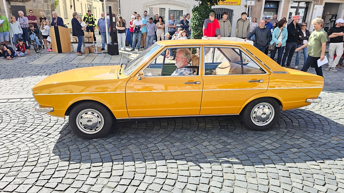 Jede Menge automobile Schätze auf dem Kemnather Stadtplatz

Ein echtes Paradies für Oldtimerfreunde gab es am Samstag beim großen Oldtimertreffen in Kemnath zu erleben. Ab 10 Uhr gehörte der wunderschöne historische Stadtplatz den automobilen Schätzen vergangener Jahrzehnte. Bei bestem Oldtimerwetter präsentierten sich die liebevoll gepflegten Fahrzeuge vor einer traumhaften Kulisse – und natürlich ließen sich das auch jede Menge Zuschauer nicht entgehen.

Dicht an dicht standen die Besucher entlang des Stadtplatzes, als ein Klassiker nach dem anderen zur Fahrzeugvorstellung vorfuhr. Dabei gab es nicht nur jede Menge Chrom, glänzenden Lack und den unverwechselbaren Klang alter Motoren zu bestaunen, sondern auch viel Wissenswertes zu hören.

Wie jedes Jahr hatte Elmar Högl das Mikrofon fest im Griff. Souverän und mit enormem Fachwissen stellte er die einzelnen Fahrzeuge vor, erzählte von Baujahren, Motorisierung und technischen Besonderheiten und hatte dabei immer wieder interessante Details zu den Oldtimern parat.

Und eigentlich ist Elmar Högl aus dem Kemnather Oldtimertreffen kaum wegzudenken. Er ist nicht nur die bekannte Stimme am Mikrofon, sondern zugleich Hauptorganisator und so etwas wie das „Herz“ des Treffens. Gemeinsam mit dem KEM-Verband und der Stadt Kemnath sorgt er dafür, dass die Freunde historischer Fahrzeuge Jahr für Jahr in Kemnath zusammenkommen.

Zur Fahrzeugvorstellung gehörte natürlich auch die Übergabe der Urkunden. Diese Aufgabe übernahm Hermann Schraml, unterstützt von Stefan Wöhrl.

Und besser hätte es an diesem Vormittag eigentlich kaum passen können: herrliches Wetter, ein voller Stadtplatz, viele begeisterte Zuschauer und mittendrin jede Menge automobile Zeitgeschichte auf zwei und vier Rädern.

Nach der Vorstellung blieb noch genügend Zeit, die Oldtimer aus nächster Nähe zu betrachten, mit den Besitzern ins Gespräch zu kommen und natürlich jede Menge Fotos zu machen.

Am Nachmittag wartete dann bereits der nächste Höhepunkt auf die Teilnehmer. Um 13:15 Uhr machten sich die historischen Fahrzeuge zur gemeinsamen Ausfahrt auf den Weg. Über Berndorf, Haidenaab und Weidenberg führte die Tour unter anderem nach Goldkronach, wo eine längere Rast eingelegt wurde, bevor es schließlich wieder zurück nach Kemnath ging.

Und jetzt viel Spaß beim Durchklicken durch unsere Bilder vom Kemnather Oldtimertreffen 2026!