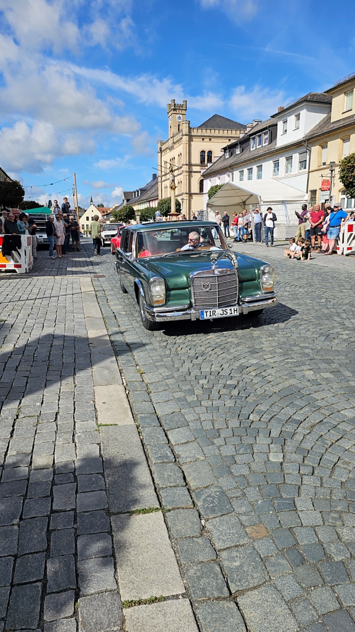 Jede Menge automobile Schätze auf dem Kemnather Stadtplatz

Ein echtes Paradies für Oldtimerfreunde gab es am Samstag beim großen Oldtimertreffen in Kemnath zu erleben. Ab 10 Uhr gehörte der wunderschöne historische Stadtplatz den automobilen Schätzen vergangener Jahrzehnte. Bei bestem Oldtimerwetter präsentierten sich die liebevoll gepflegten Fahrzeuge vor einer traumhaften Kulisse – und natürlich ließen sich das auch jede Menge Zuschauer nicht entgehen.

Dicht an dicht standen die Besucher entlang des Stadtplatzes, als ein Klassiker nach dem anderen zur Fahrzeugvorstellung vorfuhr. Dabei gab es nicht nur jede Menge Chrom, glänzenden Lack und den unverwechselbaren Klang alter Motoren zu bestaunen, sondern auch viel Wissenswertes zu hören.

Wie jedes Jahr hatte Elmar Högl das Mikrofon fest im Griff. Souverän und mit enormem Fachwissen stellte er die einzelnen Fahrzeuge vor, erzählte von Baujahren, Motorisierung und technischen Besonderheiten und hatte dabei immer wieder interessante Details zu den Oldtimern parat.

Und eigentlich ist Elmar Högl aus dem Kemnather Oldtimertreffen kaum wegzudenken. Er ist nicht nur die bekannte Stimme am Mikrofon, sondern zugleich Hauptorganisator und so etwas wie das „Herz“ des Treffens. Gemeinsam mit dem KEM-Verband und der Stadt Kemnath sorgt er dafür, dass die Freunde historischer Fahrzeuge Jahr für Jahr in Kemnath zusammenkommen.

Zur Fahrzeugvorstellung gehörte natürlich auch die Übergabe der Urkunden. Diese Aufgabe übernahm Hermann Schraml, unterstützt von Stefan Wöhrl.

Und besser hätte es an diesem Vormittag eigentlich kaum passen können: herrliches Wetter, ein voller Stadtplatz, viele begeisterte Zuschauer und mittendrin jede Menge automobile Zeitgeschichte auf zwei und vier Rädern.

Nach der Vorstellung blieb noch genügend Zeit, die Oldtimer aus nächster Nähe zu betrachten, mit den Besitzern ins Gespräch zu kommen und natürlich jede Menge Fotos zu machen.

Am Nachmittag wartete dann bereits der nächste Höhepunkt auf die Teilnehmer. Um 13:15 Uhr machten sich die historischen Fahrzeuge zur gemeinsamen Ausfahrt auf den Weg. Über Berndorf, Haidenaab und Weidenberg führte die Tour unter anderem nach Goldkronach, wo eine längere Rast eingelegt wurde, bevor es schließlich wieder zurück nach Kemnath ging.

Und jetzt viel Spaß beim Durchklicken durch unsere Bilder vom Kemnather Oldtimertreffen 2026!