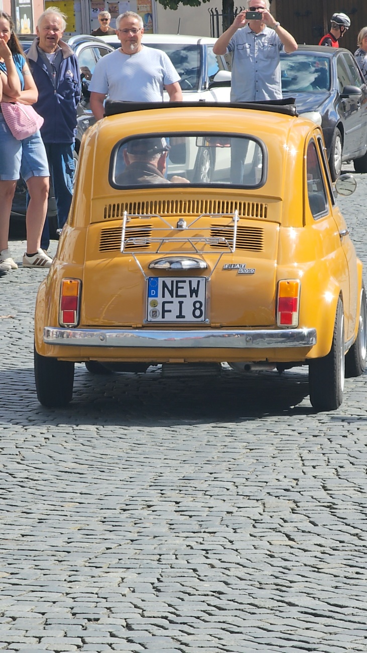 Jede Menge automobile Schätze auf dem Kemnather Stadtplatz

Ein echtes Paradies für Oldtimerfreunde gab es am Samstag beim großen Oldtimertreffen in Kemnath zu erleben. Ab 10 Uhr gehörte der wunderschöne historische Stadtplatz den automobilen Schätzen vergangener Jahrzehnte. Bei bestem Oldtimerwetter präsentierten sich die liebevoll gepflegten Fahrzeuge vor einer traumhaften Kulisse – und natürlich ließen sich das auch jede Menge Zuschauer nicht entgehen.

Dicht an dicht standen die Besucher entlang des Stadtplatzes, als ein Klassiker nach dem anderen zur Fahrzeugvorstellung vorfuhr. Dabei gab es nicht nur jede Menge Chrom, glänzenden Lack und den unverwechselbaren Klang alter Motoren zu bestaunen, sondern auch viel Wissenswertes zu hören.

Wie jedes Jahr hatte Elmar Högl das Mikrofon fest im Griff. Souverän und mit enormem Fachwissen stellte er die einzelnen Fahrzeuge vor, erzählte von Baujahren, Motorisierung und technischen Besonderheiten und hatte dabei immer wieder interessante Details zu den Oldtimern parat.

Und eigentlich ist Elmar Högl aus dem Kemnather Oldtimertreffen kaum wegzudenken. Er ist nicht nur die bekannte Stimme am Mikrofon, sondern zugleich Hauptorganisator und so etwas wie das „Herz“ des Treffens. Gemeinsam mit dem KEM-Verband und der Stadt Kemnath sorgt er dafür, dass die Freunde historischer Fahrzeuge Jahr für Jahr in Kemnath zusammenkommen.

Zur Fahrzeugvorstellung gehörte natürlich auch die Übergabe der Urkunden. Diese Aufgabe übernahm Hermann Schraml, unterstützt von Stefan Wöhrl.

Und besser hätte es an diesem Vormittag eigentlich kaum passen können: herrliches Wetter, ein voller Stadtplatz, viele begeisterte Zuschauer und mittendrin jede Menge automobile Zeitgeschichte auf zwei und vier Rädern.

Nach der Vorstellung blieb noch genügend Zeit, die Oldtimer aus nächster Nähe zu betrachten, mit den Besitzern ins Gespräch zu kommen und natürlich jede Menge Fotos zu machen.

Am Nachmittag wartete dann bereits der nächste Höhepunkt auf die Teilnehmer. Um 13:15 Uhr machten sich die historischen Fahrzeuge zur gemeinsamen Ausfahrt auf den Weg. Über Berndorf, Haidenaab und Weidenberg führte die Tour unter anderem nach Goldkronach, wo eine längere Rast eingelegt wurde, bevor es schließlich wieder zurück nach Kemnath ging.

Und jetzt viel Spaß beim Durchklicken durch unsere Bilder vom Kemnather Oldtimertreffen 2026!