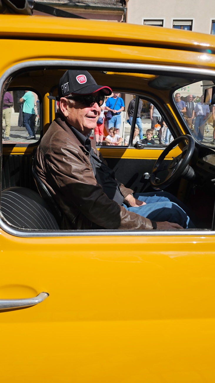 Jede Menge automobile Schätze auf dem Kemnather Stadtplatz

Ein echtes Paradies für Oldtimerfreunde gab es am Samstag beim großen Oldtimertreffen in Kemnath zu erleben. Ab 10 Uhr gehörte der wunderschöne historische Stadtplatz den automobilen Schätzen vergangener Jahrzehnte. Bei bestem Oldtimerwetter präsentierten sich die liebevoll gepflegten Fahrzeuge vor einer traumhaften Kulisse – und natürlich ließen sich das auch jede Menge Zuschauer nicht entgehen.

Dicht an dicht standen die Besucher entlang des Stadtplatzes, als ein Klassiker nach dem anderen zur Fahrzeugvorstellung vorfuhr. Dabei gab es nicht nur jede Menge Chrom, glänzenden Lack und den unverwechselbaren Klang alter Motoren zu bestaunen, sondern auch viel Wissenswertes zu hören.

Wie jedes Jahr hatte Elmar Högl das Mikrofon fest im Griff. Souverän und mit enormem Fachwissen stellte er die einzelnen Fahrzeuge vor, erzählte von Baujahren, Motorisierung und technischen Besonderheiten und hatte dabei immer wieder interessante Details zu den Oldtimern parat.

Und eigentlich ist Elmar Högl aus dem Kemnather Oldtimertreffen kaum wegzudenken. Er ist nicht nur die bekannte Stimme am Mikrofon, sondern zugleich Hauptorganisator und so etwas wie das „Herz“ des Treffens. Gemeinsam mit dem KEM-Verband und der Stadt Kemnath sorgt er dafür, dass die Freunde historischer Fahrzeuge Jahr für Jahr in Kemnath zusammenkommen.

Zur Fahrzeugvorstellung gehörte natürlich auch die Übergabe der Urkunden. Diese Aufgabe übernahm Hermann Schraml, unterstützt von Stefan Wöhrl.

Und besser hätte es an diesem Vormittag eigentlich kaum passen können: herrliches Wetter, ein voller Stadtplatz, viele begeisterte Zuschauer und mittendrin jede Menge automobile Zeitgeschichte auf zwei und vier Rädern.

Nach der Vorstellung blieb noch genügend Zeit, die Oldtimer aus nächster Nähe zu betrachten, mit den Besitzern ins Gespräch zu kommen und natürlich jede Menge Fotos zu machen.

Am Nachmittag wartete dann bereits der nächste Höhepunkt auf die Teilnehmer. Um 13:15 Uhr machten sich die historischen Fahrzeuge zur gemeinsamen Ausfahrt auf den Weg. Über Berndorf, Haidenaab und Weidenberg führte die Tour unter anderem nach Goldkronach, wo eine längere Rast eingelegt wurde, bevor es schließlich wieder zurück nach Kemnath ging.

Und jetzt viel Spaß beim Durchklicken durch unsere Bilder vom Kemnather Oldtimertreffen 2026!