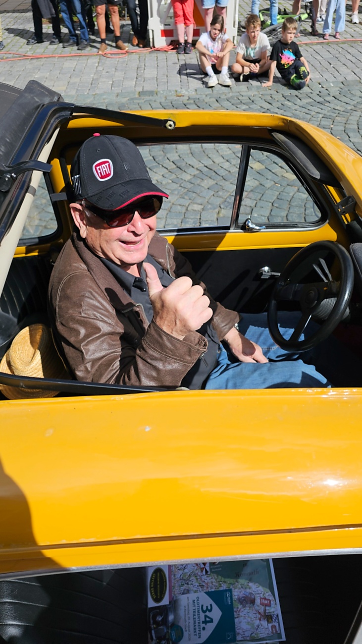 Jede Menge automobile Schätze auf dem Kemnather Stadtplatz

Ein echtes Paradies für Oldtimerfreunde gab es am Samstag beim großen Oldtimertreffen in Kemnath zu erleben. Ab 10 Uhr gehörte der wunderschöne historische Stadtplatz den automobilen Schätzen vergangener Jahrzehnte. Bei bestem Oldtimerwetter präsentierten sich die liebevoll gepflegten Fahrzeuge vor einer traumhaften Kulisse – und natürlich ließen sich das auch jede Menge Zuschauer nicht entgehen.

Dicht an dicht standen die Besucher entlang des Stadtplatzes, als ein Klassiker nach dem anderen zur Fahrzeugvorstellung vorfuhr. Dabei gab es nicht nur jede Menge Chrom, glänzenden Lack und den unverwechselbaren Klang alter Motoren zu bestaunen, sondern auch viel Wissenswertes zu hören.

Wie jedes Jahr hatte Elmar Högl das Mikrofon fest im Griff. Souverän und mit enormem Fachwissen stellte er die einzelnen Fahrzeuge vor, erzählte von Baujahren, Motorisierung und technischen Besonderheiten und hatte dabei immer wieder interessante Details zu den Oldtimern parat.

Und eigentlich ist Elmar Högl aus dem Kemnather Oldtimertreffen kaum wegzudenken. Er ist nicht nur die bekannte Stimme am Mikrofon, sondern zugleich Hauptorganisator und so etwas wie das „Herz“ des Treffens. Gemeinsam mit dem KEM-Verband und der Stadt Kemnath sorgt er dafür, dass die Freunde historischer Fahrzeuge Jahr für Jahr in Kemnath zusammenkommen.

Zur Fahrzeugvorstellung gehörte natürlich auch die Übergabe der Urkunden. Diese Aufgabe übernahm Hermann Schraml, unterstützt von Stefan Wöhrl.

Und besser hätte es an diesem Vormittag eigentlich kaum passen können: herrliches Wetter, ein voller Stadtplatz, viele begeisterte Zuschauer und mittendrin jede Menge automobile Zeitgeschichte auf zwei und vier Rädern.

Nach der Vorstellung blieb noch genügend Zeit, die Oldtimer aus nächster Nähe zu betrachten, mit den Besitzern ins Gespräch zu kommen und natürlich jede Menge Fotos zu machen.

Am Nachmittag wartete dann bereits der nächste Höhepunkt auf die Teilnehmer. Um 13:15 Uhr machten sich die historischen Fahrzeuge zur gemeinsamen Ausfahrt auf den Weg. Über Berndorf, Haidenaab und Weidenberg führte die Tour unter anderem nach Goldkronach, wo eine längere Rast eingelegt wurde, bevor es schließlich wieder zurück nach Kemnath ging.

Und jetzt viel Spaß beim Durchklicken durch unsere Bilder vom Kemnather Oldtimertreffen 2026!