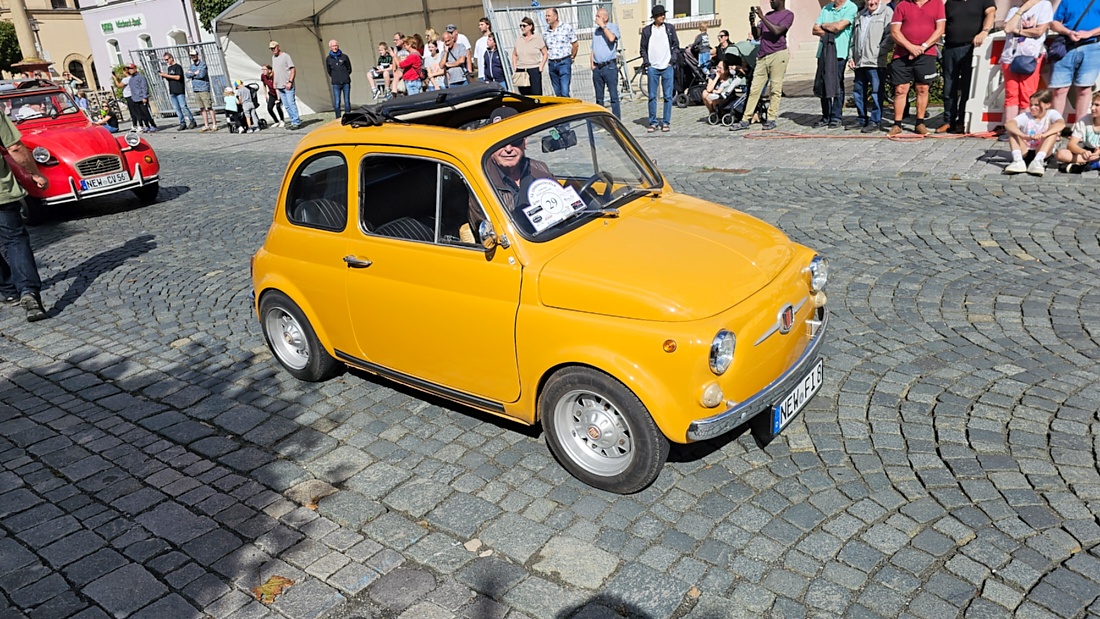 Jede Menge automobile Schätze auf dem Kemnather Stadtplatz

Ein echtes Paradies für Oldtimerfreunde gab es am Samstag beim großen Oldtimertreffen in Kemnath zu erleben. Ab 10 Uhr gehörte der wunderschöne historische Stadtplatz den automobilen Schätzen vergangener Jahrzehnte. Bei bestem Oldtimerwetter präsentierten sich die liebevoll gepflegten Fahrzeuge vor einer traumhaften Kulisse – und natürlich ließen sich das auch jede Menge Zuschauer nicht entgehen.

Dicht an dicht standen die Besucher entlang des Stadtplatzes, als ein Klassiker nach dem anderen zur Fahrzeugvorstellung vorfuhr. Dabei gab es nicht nur jede Menge Chrom, glänzenden Lack und den unverwechselbaren Klang alter Motoren zu bestaunen, sondern auch viel Wissenswertes zu hören.

Wie jedes Jahr hatte Elmar Högl das Mikrofon fest im Griff. Souverän und mit enormem Fachwissen stellte er die einzelnen Fahrzeuge vor, erzählte von Baujahren, Motorisierung und technischen Besonderheiten und hatte dabei immer wieder interessante Details zu den Oldtimern parat.

Und eigentlich ist Elmar Högl aus dem Kemnather Oldtimertreffen kaum wegzudenken. Er ist nicht nur die bekannte Stimme am Mikrofon, sondern zugleich Hauptorganisator und so etwas wie das „Herz“ des Treffens. Gemeinsam mit dem KEM-Verband und der Stadt Kemnath sorgt er dafür, dass die Freunde historischer Fahrzeuge Jahr für Jahr in Kemnath zusammenkommen.

Zur Fahrzeugvorstellung gehörte natürlich auch die Übergabe der Urkunden. Diese Aufgabe übernahm Hermann Schraml, unterstützt von Stefan Wöhrl.

Und besser hätte es an diesem Vormittag eigentlich kaum passen können: herrliches Wetter, ein voller Stadtplatz, viele begeisterte Zuschauer und mittendrin jede Menge automobile Zeitgeschichte auf zwei und vier Rädern.

Nach der Vorstellung blieb noch genügend Zeit, die Oldtimer aus nächster Nähe zu betrachten, mit den Besitzern ins Gespräch zu kommen und natürlich jede Menge Fotos zu machen.

Am Nachmittag wartete dann bereits der nächste Höhepunkt auf die Teilnehmer. Um 13:15 Uhr machten sich die historischen Fahrzeuge zur gemeinsamen Ausfahrt auf den Weg. Über Berndorf, Haidenaab und Weidenberg führte die Tour unter anderem nach Goldkronach, wo eine längere Rast eingelegt wurde, bevor es schließlich wieder zurück nach Kemnath ging.

Und jetzt viel Spaß beim Durchklicken durch unsere Bilder vom Kemnather Oldtimertreffen 2026!