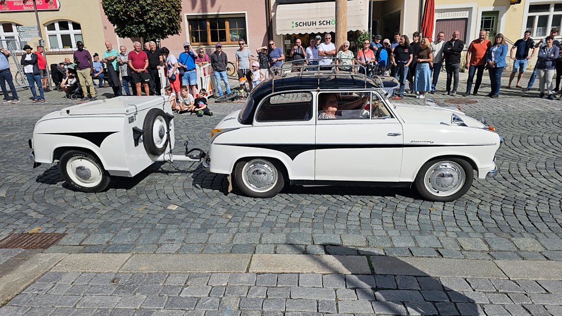 Jede Menge automobile Schätze auf dem Kemnather Stadtplatz

Ein echtes Paradies für Oldtimerfreunde gab es am Samstag beim großen Oldtimertreffen in Kemnath zu erleben. Ab 10 Uhr gehörte der wunderschöne historische Stadtplatz den automobilen Schätzen vergangener Jahrzehnte. Bei bestem Oldtimerwetter präsentierten sich die liebevoll gepflegten Fahrzeuge vor einer traumhaften Kulisse – und natürlich ließen sich das auch jede Menge Zuschauer nicht entgehen.

Dicht an dicht standen die Besucher entlang des Stadtplatzes, als ein Klassiker nach dem anderen zur Fahrzeugvorstellung vorfuhr. Dabei gab es nicht nur jede Menge Chrom, glänzenden Lack und den unverwechselbaren Klang alter Motoren zu bestaunen, sondern auch viel Wissenswertes zu hören.

Wie jedes Jahr hatte Elmar Högl das Mikrofon fest im Griff. Souverän und mit enormem Fachwissen stellte er die einzelnen Fahrzeuge vor, erzählte von Baujahren, Motorisierung und technischen Besonderheiten und hatte dabei immer wieder interessante Details zu den Oldtimern parat.

Und eigentlich ist Elmar Högl aus dem Kemnather Oldtimertreffen kaum wegzudenken. Er ist nicht nur die bekannte Stimme am Mikrofon, sondern zugleich Hauptorganisator und so etwas wie das „Herz“ des Treffens. Gemeinsam mit dem KEM-Verband und der Stadt Kemnath sorgt er dafür, dass die Freunde historischer Fahrzeuge Jahr für Jahr in Kemnath zusammenkommen.

Zur Fahrzeugvorstellung gehörte natürlich auch die Übergabe der Urkunden. Diese Aufgabe übernahm Hermann Schraml, unterstützt von Stefan Wöhrl.

Und besser hätte es an diesem Vormittag eigentlich kaum passen können: herrliches Wetter, ein voller Stadtplatz, viele begeisterte Zuschauer und mittendrin jede Menge automobile Zeitgeschichte auf zwei und vier Rädern.

Nach der Vorstellung blieb noch genügend Zeit, die Oldtimer aus nächster Nähe zu betrachten, mit den Besitzern ins Gespräch zu kommen und natürlich jede Menge Fotos zu machen.

Am Nachmittag wartete dann bereits der nächste Höhepunkt auf die Teilnehmer. Um 13:15 Uhr machten sich die historischen Fahrzeuge zur gemeinsamen Ausfahrt auf den Weg. Über Berndorf, Haidenaab und Weidenberg führte die Tour unter anderem nach Goldkronach, wo eine längere Rast eingelegt wurde, bevor es schließlich wieder zurück nach Kemnath ging.

Und jetzt viel Spaß beim Durchklicken durch unsere Bilder vom Kemnather Oldtimertreffen 2026!