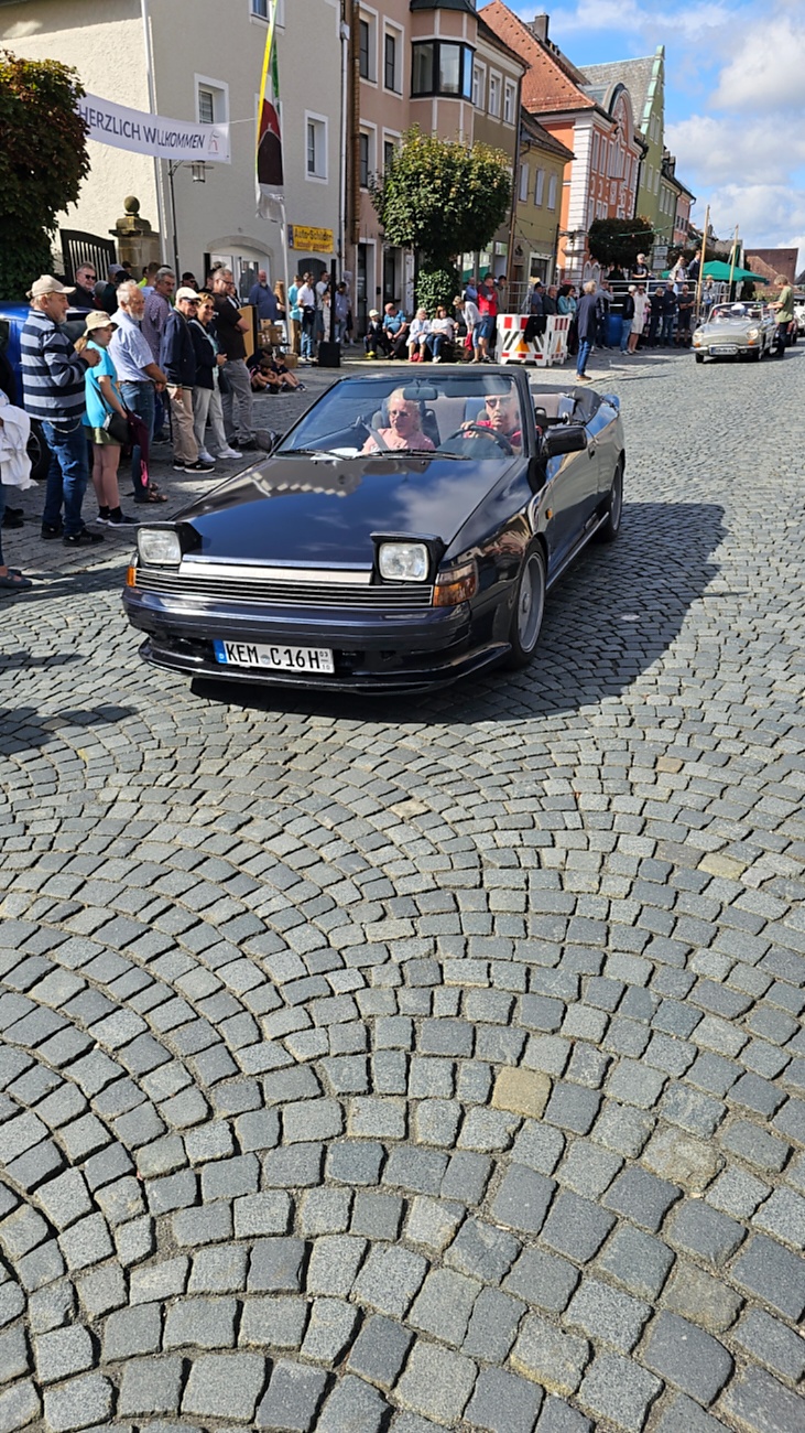 Jede Menge automobile Schätze auf dem Kemnather Stadtplatz

Ein echtes Paradies für Oldtimerfreunde gab es am Samstag beim großen Oldtimertreffen in Kemnath zu erleben. Ab 10 Uhr gehörte der wunderschöne historische Stadtplatz den automobilen Schätzen vergangener Jahrzehnte. Bei bestem Oldtimerwetter präsentierten sich die liebevoll gepflegten Fahrzeuge vor einer traumhaften Kulisse – und natürlich ließen sich das auch jede Menge Zuschauer nicht entgehen.

Dicht an dicht standen die Besucher entlang des Stadtplatzes, als ein Klassiker nach dem anderen zur Fahrzeugvorstellung vorfuhr. Dabei gab es nicht nur jede Menge Chrom, glänzenden Lack und den unverwechselbaren Klang alter Motoren zu bestaunen, sondern auch viel Wissenswertes zu hören.

Wie jedes Jahr hatte Elmar Högl das Mikrofon fest im Griff. Souverän und mit enormem Fachwissen stellte er die einzelnen Fahrzeuge vor, erzählte von Baujahren, Motorisierung und technischen Besonderheiten und hatte dabei immer wieder interessante Details zu den Oldtimern parat.

Und eigentlich ist Elmar Högl aus dem Kemnather Oldtimertreffen kaum wegzudenken. Er ist nicht nur die bekannte Stimme am Mikrofon, sondern zugleich Hauptorganisator und so etwas wie das „Herz“ des Treffens. Gemeinsam mit dem KEM-Verband und der Stadt Kemnath sorgt er dafür, dass die Freunde historischer Fahrzeuge Jahr für Jahr in Kemnath zusammenkommen.

Zur Fahrzeugvorstellung gehörte natürlich auch die Übergabe der Urkunden. Diese Aufgabe übernahm Hermann Schraml, unterstützt von Stefan Wöhrl.

Und besser hätte es an diesem Vormittag eigentlich kaum passen können: herrliches Wetter, ein voller Stadtplatz, viele begeisterte Zuschauer und mittendrin jede Menge automobile Zeitgeschichte auf zwei und vier Rädern.

Nach der Vorstellung blieb noch genügend Zeit, die Oldtimer aus nächster Nähe zu betrachten, mit den Besitzern ins Gespräch zu kommen und natürlich jede Menge Fotos zu machen.

Am Nachmittag wartete dann bereits der nächste Höhepunkt auf die Teilnehmer. Um 13:15 Uhr machten sich die historischen Fahrzeuge zur gemeinsamen Ausfahrt auf den Weg. Über Berndorf, Haidenaab und Weidenberg führte die Tour unter anderem nach Goldkronach, wo eine längere Rast eingelegt wurde, bevor es schließlich wieder zurück nach Kemnath ging.

Und jetzt viel Spaß beim Durchklicken durch unsere Bilder vom Kemnather Oldtimertreffen 2026!