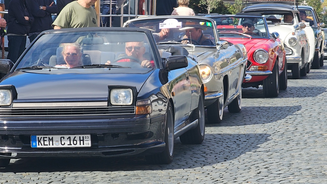 Jede Menge automobile Schätze auf dem Kemnather Stadtplatz

Ein echtes Paradies für Oldtimerfreunde gab es am Samstag beim großen Oldtimertreffen in Kemnath zu erleben. Ab 10 Uhr gehörte der wunderschöne historische Stadtplatz den automobilen Schätzen vergangener Jahrzehnte. Bei bestem Oldtimerwetter präsentierten sich die liebevoll gepflegten Fahrzeuge vor einer traumhaften Kulisse – und natürlich ließen sich das auch jede Menge Zuschauer nicht entgehen.

Dicht an dicht standen die Besucher entlang des Stadtplatzes, als ein Klassiker nach dem anderen zur Fahrzeugvorstellung vorfuhr. Dabei gab es nicht nur jede Menge Chrom, glänzenden Lack und den unverwechselbaren Klang alter Motoren zu bestaunen, sondern auch viel Wissenswertes zu hören.

Wie jedes Jahr hatte Elmar Högl das Mikrofon fest im Griff. Souverän und mit enormem Fachwissen stellte er die einzelnen Fahrzeuge vor, erzählte von Baujahren, Motorisierung und technischen Besonderheiten und hatte dabei immer wieder interessante Details zu den Oldtimern parat.

Und eigentlich ist Elmar Högl aus dem Kemnather Oldtimertreffen kaum wegzudenken. Er ist nicht nur die bekannte Stimme am Mikrofon, sondern zugleich Hauptorganisator und so etwas wie das „Herz“ des Treffens. Gemeinsam mit dem KEM-Verband und der Stadt Kemnath sorgt er dafür, dass die Freunde historischer Fahrzeuge Jahr für Jahr in Kemnath zusammenkommen.

Zur Fahrzeugvorstellung gehörte natürlich auch die Übergabe der Urkunden. Diese Aufgabe übernahm Hermann Schraml, unterstützt von Stefan Wöhrl.

Und besser hätte es an diesem Vormittag eigentlich kaum passen können: herrliches Wetter, ein voller Stadtplatz, viele begeisterte Zuschauer und mittendrin jede Menge automobile Zeitgeschichte auf zwei und vier Rädern.

Nach der Vorstellung blieb noch genügend Zeit, die Oldtimer aus nächster Nähe zu betrachten, mit den Besitzern ins Gespräch zu kommen und natürlich jede Menge Fotos zu machen.

Am Nachmittag wartete dann bereits der nächste Höhepunkt auf die Teilnehmer. Um 13:15 Uhr machten sich die historischen Fahrzeuge zur gemeinsamen Ausfahrt auf den Weg. Über Berndorf, Haidenaab und Weidenberg führte die Tour unter anderem nach Goldkronach, wo eine längere Rast eingelegt wurde, bevor es schließlich wieder zurück nach Kemnath ging.

Und jetzt viel Spaß beim Durchklicken durch unsere Bilder vom Kemnather Oldtimertreffen 2026!