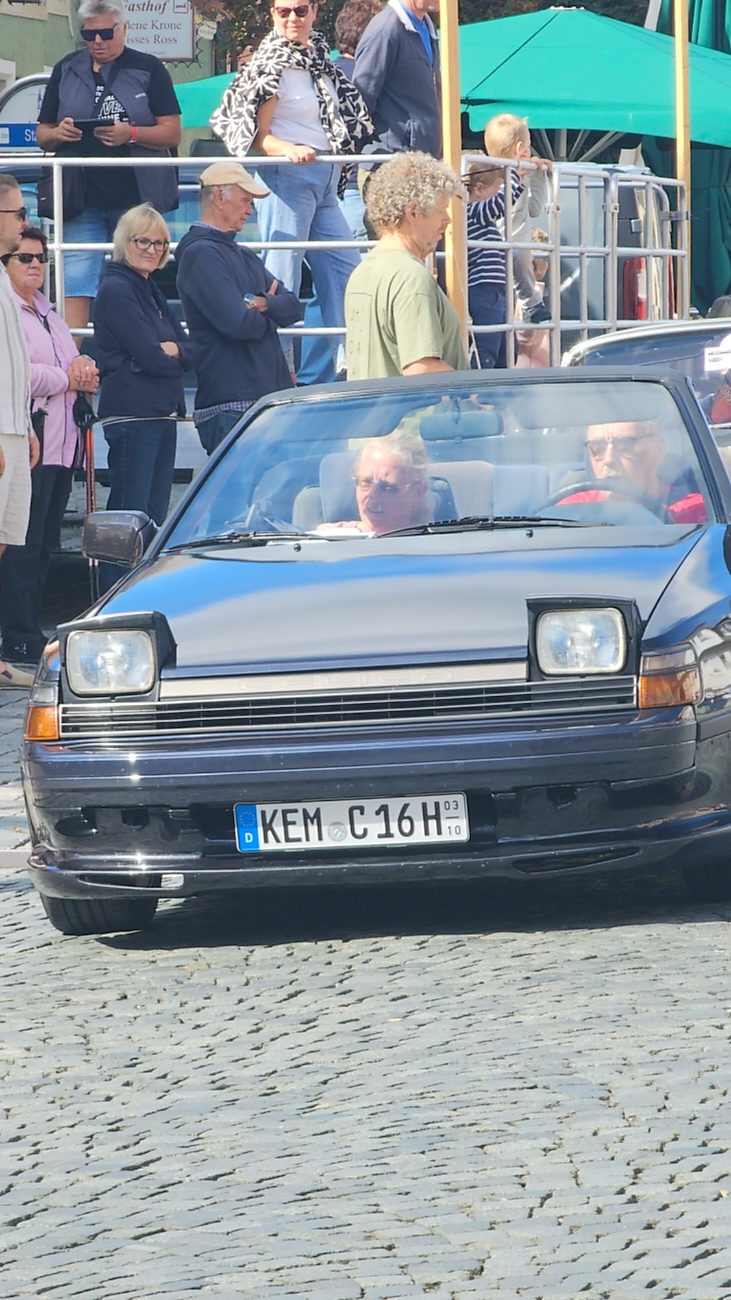 Jede Menge automobile Schätze auf dem Kemnather Stadtplatz

Ein echtes Paradies für Oldtimerfreunde gab es am Samstag beim großen Oldtimertreffen in Kemnath zu erleben. Ab 10 Uhr gehörte der wunderschöne historische Stadtplatz den automobilen Schätzen vergangener Jahrzehnte. Bei bestem Oldtimerwetter präsentierten sich die liebevoll gepflegten Fahrzeuge vor einer traumhaften Kulisse – und natürlich ließen sich das auch jede Menge Zuschauer nicht entgehen.

Dicht an dicht standen die Besucher entlang des Stadtplatzes, als ein Klassiker nach dem anderen zur Fahrzeugvorstellung vorfuhr. Dabei gab es nicht nur jede Menge Chrom, glänzenden Lack und den unverwechselbaren Klang alter Motoren zu bestaunen, sondern auch viel Wissenswertes zu hören.

Wie jedes Jahr hatte Elmar Högl das Mikrofon fest im Griff. Souverän und mit enormem Fachwissen stellte er die einzelnen Fahrzeuge vor, erzählte von Baujahren, Motorisierung und technischen Besonderheiten und hatte dabei immer wieder interessante Details zu den Oldtimern parat.

Und eigentlich ist Elmar Högl aus dem Kemnather Oldtimertreffen kaum wegzudenken. Er ist nicht nur die bekannte Stimme am Mikrofon, sondern zugleich Hauptorganisator und so etwas wie das „Herz“ des Treffens. Gemeinsam mit dem KEM-Verband und der Stadt Kemnath sorgt er dafür, dass die Freunde historischer Fahrzeuge Jahr für Jahr in Kemnath zusammenkommen.

Zur Fahrzeugvorstellung gehörte natürlich auch die Übergabe der Urkunden. Diese Aufgabe übernahm Hermann Schraml, unterstützt von Stefan Wöhrl.

Und besser hätte es an diesem Vormittag eigentlich kaum passen können: herrliches Wetter, ein voller Stadtplatz, viele begeisterte Zuschauer und mittendrin jede Menge automobile Zeitgeschichte auf zwei und vier Rädern.

Nach der Vorstellung blieb noch genügend Zeit, die Oldtimer aus nächster Nähe zu betrachten, mit den Besitzern ins Gespräch zu kommen und natürlich jede Menge Fotos zu machen.

Am Nachmittag wartete dann bereits der nächste Höhepunkt auf die Teilnehmer. Um 13:15 Uhr machten sich die historischen Fahrzeuge zur gemeinsamen Ausfahrt auf den Weg. Über Berndorf, Haidenaab und Weidenberg führte die Tour unter anderem nach Goldkronach, wo eine längere Rast eingelegt wurde, bevor es schließlich wieder zurück nach Kemnath ging.

Und jetzt viel Spaß beim Durchklicken durch unsere Bilder vom Kemnather Oldtimertreffen 2026!