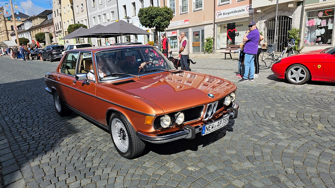 Jede Menge automobile Schätze auf dem Kemnather Stadtplatz

Ein echtes Paradies für Oldtimerfreunde gab es am Samstag beim großen Oldtimertreffen in Kemnath zu erleben. Ab 10 Uhr gehörte der wunderschöne historische Stadtplatz den automobilen Schätzen vergangener Jahrzehnte. Bei bestem Oldtimerwetter präsentierten sich die liebevoll gepflegten Fahrzeuge vor einer traumhaften Kulisse – und natürlich ließen sich das auch jede Menge Zuschauer nicht entgehen.

Dicht an dicht standen die Besucher entlang des Stadtplatzes, als ein Klassiker nach dem anderen zur Fahrzeugvorstellung vorfuhr. Dabei gab es nicht nur jede Menge Chrom, glänzenden Lack und den unverwechselbaren Klang alter Motoren zu bestaunen, sondern auch viel Wissenswertes zu hören.

Wie jedes Jahr hatte Elmar Högl das Mikrofon fest im Griff. Souverän und mit enormem Fachwissen stellte er die einzelnen Fahrzeuge vor, erzählte von Baujahren, Motorisierung und technischen Besonderheiten und hatte dabei immer wieder interessante Details zu den Oldtimern parat.

Und eigentlich ist Elmar Högl aus dem Kemnather Oldtimertreffen kaum wegzudenken. Er ist nicht nur die bekannte Stimme am Mikrofon, sondern zugleich Hauptorganisator und so etwas wie das „Herz“ des Treffens. Gemeinsam mit dem KEM-Verband und der Stadt Kemnath sorgt er dafür, dass die Freunde historischer Fahrzeuge Jahr für Jahr in Kemnath zusammenkommen.

Zur Fahrzeugvorstellung gehörte natürlich auch die Übergabe der Urkunden. Diese Aufgabe übernahm Hermann Schraml, unterstützt von Stefan Wöhrl.

Und besser hätte es an diesem Vormittag eigentlich kaum passen können: herrliches Wetter, ein voller Stadtplatz, viele begeisterte Zuschauer und mittendrin jede Menge automobile Zeitgeschichte auf zwei und vier Rädern.

Nach der Vorstellung blieb noch genügend Zeit, die Oldtimer aus nächster Nähe zu betrachten, mit den Besitzern ins Gespräch zu kommen und natürlich jede Menge Fotos zu machen.

Am Nachmittag wartete dann bereits der nächste Höhepunkt auf die Teilnehmer. Um 13:15 Uhr machten sich die historischen Fahrzeuge zur gemeinsamen Ausfahrt auf den Weg. Über Berndorf, Haidenaab und Weidenberg führte die Tour unter anderem nach Goldkronach, wo eine längere Rast eingelegt wurde, bevor es schließlich wieder zurück nach Kemnath ging.

Und jetzt viel Spaß beim Durchklicken durch unsere Bilder vom Kemnather Oldtimertreffen 2026!