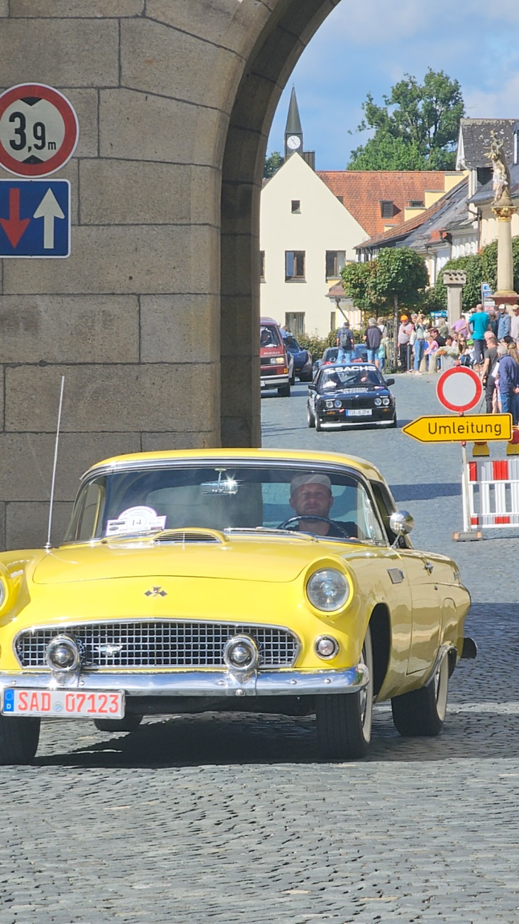 Jede Menge automobile Schätze auf dem Kemnather Stadtplatz

Ein echtes Paradies für Oldtimerfreunde gab es am Samstag beim großen Oldtimertreffen in Kemnath zu erleben. Ab 10 Uhr gehörte der wunderschöne historische Stadtplatz den automobilen Schätzen vergangener Jahrzehnte. Bei bestem Oldtimerwetter präsentierten sich die liebevoll gepflegten Fahrzeuge vor einer traumhaften Kulisse – und natürlich ließen sich das auch jede Menge Zuschauer nicht entgehen.

Dicht an dicht standen die Besucher entlang des Stadtplatzes, als ein Klassiker nach dem anderen zur Fahrzeugvorstellung vorfuhr. Dabei gab es nicht nur jede Menge Chrom, glänzenden Lack und den unverwechselbaren Klang alter Motoren zu bestaunen, sondern auch viel Wissenswertes zu hören.

Wie jedes Jahr hatte Elmar Högl das Mikrofon fest im Griff. Souverän und mit enormem Fachwissen stellte er die einzelnen Fahrzeuge vor, erzählte von Baujahren, Motorisierung und technischen Besonderheiten und hatte dabei immer wieder interessante Details zu den Oldtimern parat.

Und eigentlich ist Elmar Högl aus dem Kemnather Oldtimertreffen kaum wegzudenken. Er ist nicht nur die bekannte Stimme am Mikrofon, sondern zugleich Hauptorganisator und so etwas wie das „Herz“ des Treffens. Gemeinsam mit dem KEM-Verband und der Stadt Kemnath sorgt er dafür, dass die Freunde historischer Fahrzeuge Jahr für Jahr in Kemnath zusammenkommen.

Zur Fahrzeugvorstellung gehörte natürlich auch die Übergabe der Urkunden. Diese Aufgabe übernahm Hermann Schraml, unterstützt von Stefan Wöhrl.

Und besser hätte es an diesem Vormittag eigentlich kaum passen können: herrliches Wetter, ein voller Stadtplatz, viele begeisterte Zuschauer und mittendrin jede Menge automobile Zeitgeschichte auf zwei und vier Rädern.

Nach der Vorstellung blieb noch genügend Zeit, die Oldtimer aus nächster Nähe zu betrachten, mit den Besitzern ins Gespräch zu kommen und natürlich jede Menge Fotos zu machen.

Am Nachmittag wartete dann bereits der nächste Höhepunkt auf die Teilnehmer. Um 13:15 Uhr machten sich die historischen Fahrzeuge zur gemeinsamen Ausfahrt auf den Weg. Über Berndorf, Haidenaab und Weidenberg führte die Tour unter anderem nach Goldkronach, wo eine längere Rast eingelegt wurde, bevor es schließlich wieder zurück nach Kemnath ging.

Und jetzt viel Spaß beim Durchklicken durch unsere Bilder vom Kemnather Oldtimertreffen 2026!