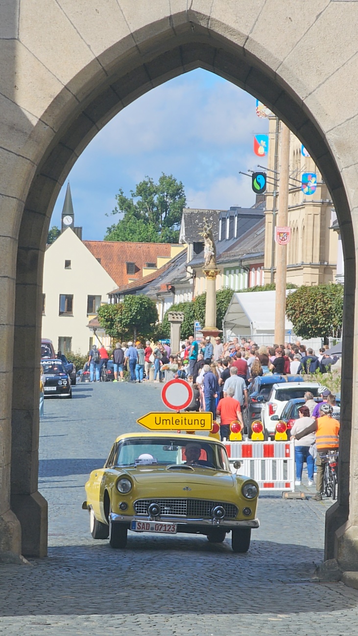 Jede Menge automobile Schätze auf dem Kemnather Stadtplatz

Ein echtes Paradies für Oldtimerfreunde gab es am Samstag beim großen Oldtimertreffen in Kemnath zu erleben. Ab 10 Uhr gehörte der wunderschöne historische Stadtplatz den automobilen Schätzen vergangener Jahrzehnte. Bei bestem Oldtimerwetter präsentierten sich die liebevoll gepflegten Fahrzeuge vor einer traumhaften Kulisse – und natürlich ließen sich das auch jede Menge Zuschauer nicht entgehen.

Dicht an dicht standen die Besucher entlang des Stadtplatzes, als ein Klassiker nach dem anderen zur Fahrzeugvorstellung vorfuhr. Dabei gab es nicht nur jede Menge Chrom, glänzenden Lack und den unverwechselbaren Klang alter Motoren zu bestaunen, sondern auch viel Wissenswertes zu hören.

Wie jedes Jahr hatte Elmar Högl das Mikrofon fest im Griff. Souverän und mit enormem Fachwissen stellte er die einzelnen Fahrzeuge vor, erzählte von Baujahren, Motorisierung und technischen Besonderheiten und hatte dabei immer wieder interessante Details zu den Oldtimern parat.

Und eigentlich ist Elmar Högl aus dem Kemnather Oldtimertreffen kaum wegzudenken. Er ist nicht nur die bekannte Stimme am Mikrofon, sondern zugleich Hauptorganisator und so etwas wie das „Herz“ des Treffens. Gemeinsam mit dem KEM-Verband und der Stadt Kemnath sorgt er dafür, dass die Freunde historischer Fahrzeuge Jahr für Jahr in Kemnath zusammenkommen.

Zur Fahrzeugvorstellung gehörte natürlich auch die Übergabe der Urkunden. Diese Aufgabe übernahm Hermann Schraml, unterstützt von Stefan Wöhrl.

Und besser hätte es an diesem Vormittag eigentlich kaum passen können: herrliches Wetter, ein voller Stadtplatz, viele begeisterte Zuschauer und mittendrin jede Menge automobile Zeitgeschichte auf zwei und vier Rädern.

Nach der Vorstellung blieb noch genügend Zeit, die Oldtimer aus nächster Nähe zu betrachten, mit den Besitzern ins Gespräch zu kommen und natürlich jede Menge Fotos zu machen.

Am Nachmittag wartete dann bereits der nächste Höhepunkt auf die Teilnehmer. Um 13:15 Uhr machten sich die historischen Fahrzeuge zur gemeinsamen Ausfahrt auf den Weg. Über Berndorf, Haidenaab und Weidenberg führte die Tour unter anderem nach Goldkronach, wo eine längere Rast eingelegt wurde, bevor es schließlich wieder zurück nach Kemnath ging.

Und jetzt viel Spaß beim Durchklicken durch unsere Bilder vom Kemnather Oldtimertreffen 2026!