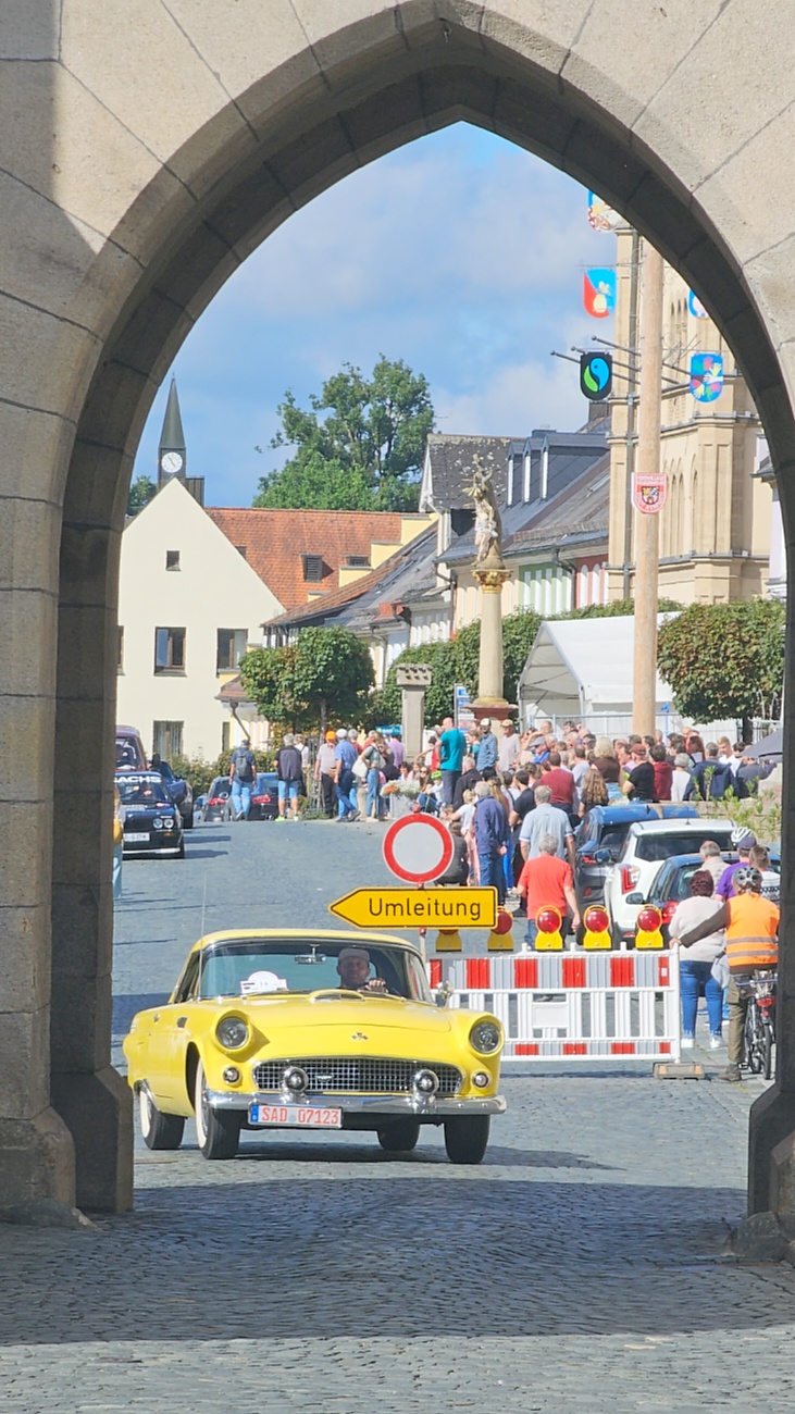 Jede Menge automobile Schätze auf dem Kemnather Stadtplatz

Ein echtes Paradies für Oldtimerfreunde gab es am Samstag beim großen Oldtimertreffen in Kemnath zu erleben. Ab 10 Uhr gehörte der wunderschöne historische Stadtplatz den automobilen Schätzen vergangener Jahrzehnte. Bei bestem Oldtimerwetter präsentierten sich die liebevoll gepflegten Fahrzeuge vor einer traumhaften Kulisse – und natürlich ließen sich das auch jede Menge Zuschauer nicht entgehen.

Dicht an dicht standen die Besucher entlang des Stadtplatzes, als ein Klassiker nach dem anderen zur Fahrzeugvorstellung vorfuhr. Dabei gab es nicht nur jede Menge Chrom, glänzenden Lack und den unverwechselbaren Klang alter Motoren zu bestaunen, sondern auch viel Wissenswertes zu hören.

Wie jedes Jahr hatte Elmar Högl das Mikrofon fest im Griff. Souverän und mit enormem Fachwissen stellte er die einzelnen Fahrzeuge vor, erzählte von Baujahren, Motorisierung und technischen Besonderheiten und hatte dabei immer wieder interessante Details zu den Oldtimern parat.

Und eigentlich ist Elmar Högl aus dem Kemnather Oldtimertreffen kaum wegzudenken. Er ist nicht nur die bekannte Stimme am Mikrofon, sondern zugleich Hauptorganisator und so etwas wie das „Herz“ des Treffens. Gemeinsam mit dem KEM-Verband und der Stadt Kemnath sorgt er dafür, dass die Freunde historischer Fahrzeuge Jahr für Jahr in Kemnath zusammenkommen.

Zur Fahrzeugvorstellung gehörte natürlich auch die Übergabe der Urkunden. Diese Aufgabe übernahm Hermann Schraml, unterstützt von Stefan Wöhrl.

Und besser hätte es an diesem Vormittag eigentlich kaum passen können: herrliches Wetter, ein voller Stadtplatz, viele begeisterte Zuschauer und mittendrin jede Menge automobile Zeitgeschichte auf zwei und vier Rädern.

Nach der Vorstellung blieb noch genügend Zeit, die Oldtimer aus nächster Nähe zu betrachten, mit den Besitzern ins Gespräch zu kommen und natürlich jede Menge Fotos zu machen.

Am Nachmittag wartete dann bereits der nächste Höhepunkt auf die Teilnehmer. Um 13:15 Uhr machten sich die historischen Fahrzeuge zur gemeinsamen Ausfahrt auf den Weg. Über Berndorf, Haidenaab und Weidenberg führte die Tour unter anderem nach Goldkronach, wo eine längere Rast eingelegt wurde, bevor es schließlich wieder zurück nach Kemnath ging.

Und jetzt viel Spaß beim Durchklicken durch unsere Bilder vom Kemnather Oldtimertreffen 2026!