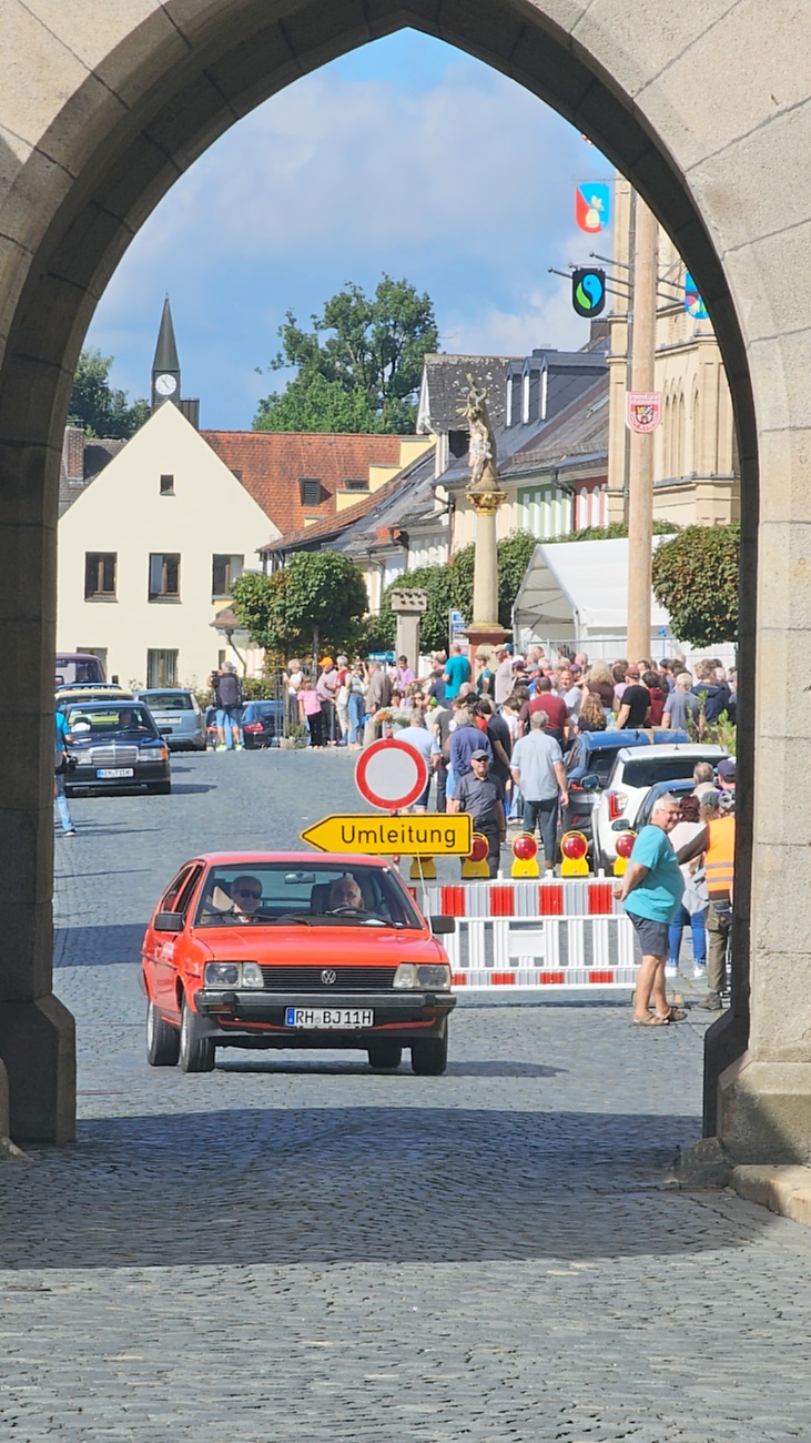 Jede Menge automobile Schätze auf dem Kemnather Stadtplatz

Ein echtes Paradies für Oldtimerfreunde gab es am Samstag beim großen Oldtimertreffen in Kemnath zu erleben. Ab 10 Uhr gehörte der wunderschöne historische Stadtplatz den automobilen Schätzen vergangener Jahrzehnte. Bei bestem Oldtimerwetter präsentierten sich die liebevoll gepflegten Fahrzeuge vor einer traumhaften Kulisse – und natürlich ließen sich das auch jede Menge Zuschauer nicht entgehen.

Dicht an dicht standen die Besucher entlang des Stadtplatzes, als ein Klassiker nach dem anderen zur Fahrzeugvorstellung vorfuhr. Dabei gab es nicht nur jede Menge Chrom, glänzenden Lack und den unverwechselbaren Klang alter Motoren zu bestaunen, sondern auch viel Wissenswertes zu hören.

Wie jedes Jahr hatte Elmar Högl das Mikrofon fest im Griff. Souverän und mit enormem Fachwissen stellte er die einzelnen Fahrzeuge vor, erzählte von Baujahren, Motorisierung und technischen Besonderheiten und hatte dabei immer wieder interessante Details zu den Oldtimern parat.

Und eigentlich ist Elmar Högl aus dem Kemnather Oldtimertreffen kaum wegzudenken. Er ist nicht nur die bekannte Stimme am Mikrofon, sondern zugleich Hauptorganisator und so etwas wie das „Herz“ des Treffens. Gemeinsam mit dem KEM-Verband und der Stadt Kemnath sorgt er dafür, dass die Freunde historischer Fahrzeuge Jahr für Jahr in Kemnath zusammenkommen.

Zur Fahrzeugvorstellung gehörte natürlich auch die Übergabe der Urkunden. Diese Aufgabe übernahm Hermann Schraml, unterstützt von Stefan Wöhrl.

Und besser hätte es an diesem Vormittag eigentlich kaum passen können: herrliches Wetter, ein voller Stadtplatz, viele begeisterte Zuschauer und mittendrin jede Menge automobile Zeitgeschichte auf zwei und vier Rädern.

Nach der Vorstellung blieb noch genügend Zeit, die Oldtimer aus nächster Nähe zu betrachten, mit den Besitzern ins Gespräch zu kommen und natürlich jede Menge Fotos zu machen.

Am Nachmittag wartete dann bereits der nächste Höhepunkt auf die Teilnehmer. Um 13:15 Uhr machten sich die historischen Fahrzeuge zur gemeinsamen Ausfahrt auf den Weg. Über Berndorf, Haidenaab und Weidenberg führte die Tour unter anderem nach Goldkronach, wo eine längere Rast eingelegt wurde, bevor es schließlich wieder zurück nach Kemnath ging.

Und jetzt viel Spaß beim Durchklicken durch unsere Bilder vom Kemnather Oldtimertreffen 2026!