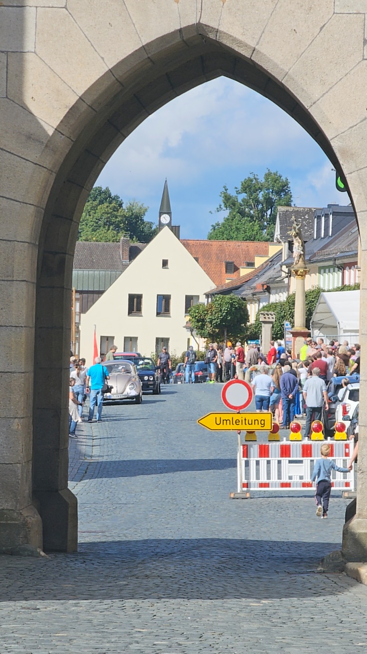 Jede Menge automobile Schätze auf dem Kemnather Stadtplatz

Ein echtes Paradies für Oldtimerfreunde gab es am Samstag beim großen Oldtimertreffen in Kemnath zu erleben. Ab 10 Uhr gehörte der wunderschöne historische Stadtplatz den automobilen Schätzen vergangener Jahrzehnte. Bei bestem Oldtimerwetter präsentierten sich die liebevoll gepflegten Fahrzeuge vor einer traumhaften Kulisse – und natürlich ließen sich das auch jede Menge Zuschauer nicht entgehen.

Dicht an dicht standen die Besucher entlang des Stadtplatzes, als ein Klassiker nach dem anderen zur Fahrzeugvorstellung vorfuhr. Dabei gab es nicht nur jede Menge Chrom, glänzenden Lack und den unverwechselbaren Klang alter Motoren zu bestaunen, sondern auch viel Wissenswertes zu hören.

Wie jedes Jahr hatte Elmar Högl das Mikrofon fest im Griff. Souverän und mit enormem Fachwissen stellte er die einzelnen Fahrzeuge vor, erzählte von Baujahren, Motorisierung und technischen Besonderheiten und hatte dabei immer wieder interessante Details zu den Oldtimern parat.

Und eigentlich ist Elmar Högl aus dem Kemnather Oldtimertreffen kaum wegzudenken. Er ist nicht nur die bekannte Stimme am Mikrofon, sondern zugleich Hauptorganisator und so etwas wie das „Herz“ des Treffens. Gemeinsam mit dem KEM-Verband und der Stadt Kemnath sorgt er dafür, dass die Freunde historischer Fahrzeuge Jahr für Jahr in Kemnath zusammenkommen.

Zur Fahrzeugvorstellung gehörte natürlich auch die Übergabe der Urkunden. Diese Aufgabe übernahm Hermann Schraml, unterstützt von Stefan Wöhrl.

Und besser hätte es an diesem Vormittag eigentlich kaum passen können: herrliches Wetter, ein voller Stadtplatz, viele begeisterte Zuschauer und mittendrin jede Menge automobile Zeitgeschichte auf zwei und vier Rädern.

Nach der Vorstellung blieb noch genügend Zeit, die Oldtimer aus nächster Nähe zu betrachten, mit den Besitzern ins Gespräch zu kommen und natürlich jede Menge Fotos zu machen.

Am Nachmittag wartete dann bereits der nächste Höhepunkt auf die Teilnehmer. Um 13:15 Uhr machten sich die historischen Fahrzeuge zur gemeinsamen Ausfahrt auf den Weg. Über Berndorf, Haidenaab und Weidenberg führte die Tour unter anderem nach Goldkronach, wo eine längere Rast eingelegt wurde, bevor es schließlich wieder zurück nach Kemnath ging.

Und jetzt viel Spaß beim Durchklicken durch unsere Bilder vom Kemnather Oldtimertreffen 2026!