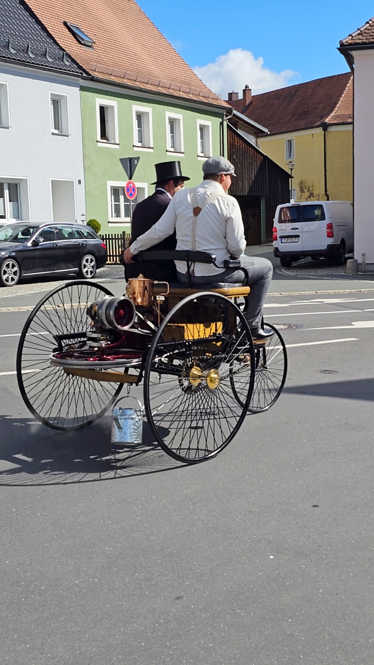 Jede Menge automobile Schätze auf dem Kemnather Stadtplatz

Ein echtes Paradies für Oldtimerfreunde gab es am Samstag beim großen Oldtimertreffen in Kemnath zu erleben. Ab 10 Uhr gehörte der wunderschöne historische Stadtplatz den automobilen Schätzen vergangener Jahrzehnte. Bei bestem Oldtimerwetter präsentierten sich die liebevoll gepflegten Fahrzeuge vor einer traumhaften Kulisse – und natürlich ließen sich das auch jede Menge Zuschauer nicht entgehen.

Dicht an dicht standen die Besucher entlang des Stadtplatzes, als ein Klassiker nach dem anderen zur Fahrzeugvorstellung vorfuhr. Dabei gab es nicht nur jede Menge Chrom, glänzenden Lack und den unverwechselbaren Klang alter Motoren zu bestaunen, sondern auch viel Wissenswertes zu hören.

Wie jedes Jahr hatte Elmar Högl das Mikrofon fest im Griff. Souverän und mit enormem Fachwissen stellte er die einzelnen Fahrzeuge vor, erzählte von Baujahren, Motorisierung und technischen Besonderheiten und hatte dabei immer wieder interessante Details zu den Oldtimern parat.

Und eigentlich ist Elmar Högl aus dem Kemnather Oldtimertreffen kaum wegzudenken. Er ist nicht nur die bekannte Stimme am Mikrofon, sondern zugleich Hauptorganisator und so etwas wie das „Herz“ des Treffens. Gemeinsam mit dem KEM-Verband und der Stadt Kemnath sorgt er dafür, dass die Freunde historischer Fahrzeuge Jahr für Jahr in Kemnath zusammenkommen.

Zur Fahrzeugvorstellung gehörte natürlich auch die Übergabe der Urkunden. Diese Aufgabe übernahm Hermann Schraml, unterstützt von Stefan Wöhrl.

Und besser hätte es an diesem Vormittag eigentlich kaum passen können: herrliches Wetter, ein voller Stadtplatz, viele begeisterte Zuschauer und mittendrin jede Menge automobile Zeitgeschichte auf zwei und vier Rädern.

Nach der Vorstellung blieb noch genügend Zeit, die Oldtimer aus nächster Nähe zu betrachten, mit den Besitzern ins Gespräch zu kommen und natürlich jede Menge Fotos zu machen.

Am Nachmittag wartete dann bereits der nächste Höhepunkt auf die Teilnehmer. Um 13:15 Uhr machten sich die historischen Fahrzeuge zur gemeinsamen Ausfahrt auf den Weg. Über Berndorf, Haidenaab und Weidenberg führte die Tour unter anderem nach Goldkronach, wo eine längere Rast eingelegt wurde, bevor es schließlich wieder zurück nach Kemnath ging.

Und jetzt viel Spaß beim Durchklicken durch unsere Bilder vom Kemnather Oldtimertreffen 2026!