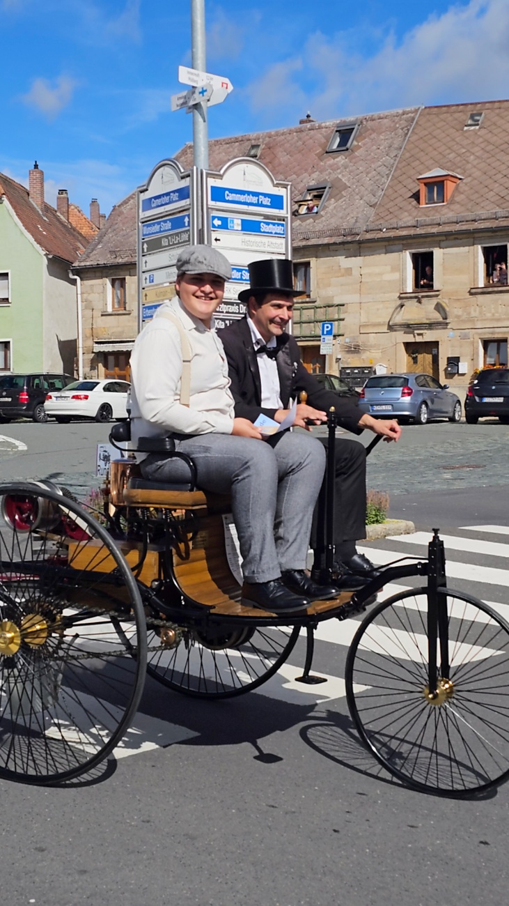 Jede Menge automobile Schätze auf dem Kemnather Stadtplatz

Ein echtes Paradies für Oldtimerfreunde gab es am Samstag beim großen Oldtimertreffen in Kemnath zu erleben. Ab 10 Uhr gehörte der wunderschöne historische Stadtplatz den automobilen Schätzen vergangener Jahrzehnte. Bei bestem Oldtimerwetter präsentierten sich die liebevoll gepflegten Fahrzeuge vor einer traumhaften Kulisse – und natürlich ließen sich das auch jede Menge Zuschauer nicht entgehen.

Dicht an dicht standen die Besucher entlang des Stadtplatzes, als ein Klassiker nach dem anderen zur Fahrzeugvorstellung vorfuhr. Dabei gab es nicht nur jede Menge Chrom, glänzenden Lack und den unverwechselbaren Klang alter Motoren zu bestaunen, sondern auch viel Wissenswertes zu hören.

Wie jedes Jahr hatte Elmar Högl das Mikrofon fest im Griff. Souverän und mit enormem Fachwissen stellte er die einzelnen Fahrzeuge vor, erzählte von Baujahren, Motorisierung und technischen Besonderheiten und hatte dabei immer wieder interessante Details zu den Oldtimern parat.

Und eigentlich ist Elmar Högl aus dem Kemnather Oldtimertreffen kaum wegzudenken. Er ist nicht nur die bekannte Stimme am Mikrofon, sondern zugleich Hauptorganisator und so etwas wie das „Herz“ des Treffens. Gemeinsam mit dem KEM-Verband und der Stadt Kemnath sorgt er dafür, dass die Freunde historischer Fahrzeuge Jahr für Jahr in Kemnath zusammenkommen.

Zur Fahrzeugvorstellung gehörte natürlich auch die Übergabe der Urkunden. Diese Aufgabe übernahm Hermann Schraml, unterstützt von Stefan Wöhrl.

Und besser hätte es an diesem Vormittag eigentlich kaum passen können: herrliches Wetter, ein voller Stadtplatz, viele begeisterte Zuschauer und mittendrin jede Menge automobile Zeitgeschichte auf zwei und vier Rädern.

Nach der Vorstellung blieb noch genügend Zeit, die Oldtimer aus nächster Nähe zu betrachten, mit den Besitzern ins Gespräch zu kommen und natürlich jede Menge Fotos zu machen.

Am Nachmittag wartete dann bereits der nächste Höhepunkt auf die Teilnehmer. Um 13:15 Uhr machten sich die historischen Fahrzeuge zur gemeinsamen Ausfahrt auf den Weg. Über Berndorf, Haidenaab und Weidenberg führte die Tour unter anderem nach Goldkronach, wo eine längere Rast eingelegt wurde, bevor es schließlich wieder zurück nach Kemnath ging.

Und jetzt viel Spaß beim Durchklicken durch unsere Bilder vom Kemnather Oldtimertreffen 2026!