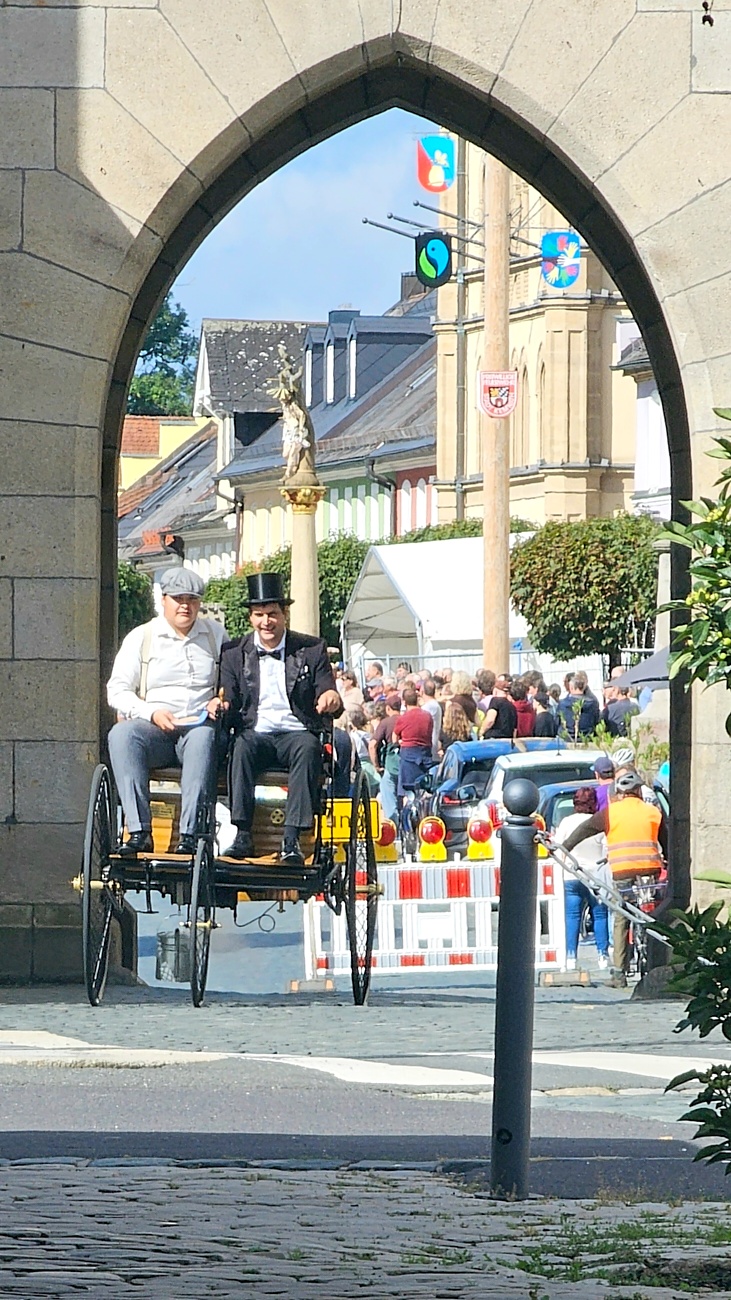Jede Menge automobile Schätze auf dem Kemnather Stadtplatz

Ein echtes Paradies für Oldtimerfreunde gab es am Samstag beim großen Oldtimertreffen in Kemnath zu erleben. Ab 10 Uhr gehörte der wunderschöne historische Stadtplatz den automobilen Schätzen vergangener Jahrzehnte. Bei bestem Oldtimerwetter präsentierten sich die liebevoll gepflegten Fahrzeuge vor einer traumhaften Kulisse – und natürlich ließen sich das auch jede Menge Zuschauer nicht entgehen.

Dicht an dicht standen die Besucher entlang des Stadtplatzes, als ein Klassiker nach dem anderen zur Fahrzeugvorstellung vorfuhr. Dabei gab es nicht nur jede Menge Chrom, glänzenden Lack und den unverwechselbaren Klang alter Motoren zu bestaunen, sondern auch viel Wissenswertes zu hören.

Wie jedes Jahr hatte Elmar Högl das Mikrofon fest im Griff. Souverän und mit enormem Fachwissen stellte er die einzelnen Fahrzeuge vor, erzählte von Baujahren, Motorisierung und technischen Besonderheiten und hatte dabei immer wieder interessante Details zu den Oldtimern parat.

Und eigentlich ist Elmar Högl aus dem Kemnather Oldtimertreffen kaum wegzudenken. Er ist nicht nur die bekannte Stimme am Mikrofon, sondern zugleich Hauptorganisator und so etwas wie das „Herz“ des Treffens. Gemeinsam mit dem KEM-Verband und der Stadt Kemnath sorgt er dafür, dass die Freunde historischer Fahrzeuge Jahr für Jahr in Kemnath zusammenkommen.

Zur Fahrzeugvorstellung gehörte natürlich auch die Übergabe der Urkunden. Diese Aufgabe übernahm Hermann Schraml, unterstützt von Stefan Wöhrl.

Und besser hätte es an diesem Vormittag eigentlich kaum passen können: herrliches Wetter, ein voller Stadtplatz, viele begeisterte Zuschauer und mittendrin jede Menge automobile Zeitgeschichte auf zwei und vier Rädern.

Nach der Vorstellung blieb noch genügend Zeit, die Oldtimer aus nächster Nähe zu betrachten, mit den Besitzern ins Gespräch zu kommen und natürlich jede Menge Fotos zu machen.

Am Nachmittag wartete dann bereits der nächste Höhepunkt auf die Teilnehmer. Um 13:15 Uhr machten sich die historischen Fahrzeuge zur gemeinsamen Ausfahrt auf den Weg. Über Berndorf, Haidenaab und Weidenberg führte die Tour unter anderem nach Goldkronach, wo eine längere Rast eingelegt wurde, bevor es schließlich wieder zurück nach Kemnath ging.

Und jetzt viel Spaß beim Durchklicken durch unsere Bilder vom Kemnather Oldtimertreffen 2026!