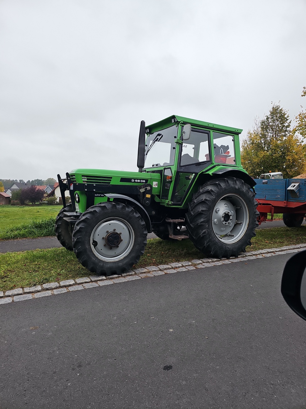 Ein kraftvoller Grünton, rundum solide Bereifung und die markante kantige Kabinenkontur machen gleich deutlich, dass hier ein historischer Ackerschlepper mit Charakter auf dem Weg steht. 

Bei der Beschriftung "D 6806“ dürfte es sich um den Deutz-Traktor D 6806 handeln, gefertigt von 1974 bis 1981 in Köln und mit einem luftgekühlten Vierzylinder-Dieselmotor mit rund 3,8l Hubraum und etwa 67PS ausgerüstet.
 
Das Getriebe dieses robusten Alltagshelfers verfügte in der Standardausführung über 12 Vorwärts- und 4 Rückwärtsgänge (typisch TW55.4, ab 1978 optional TW56.10 mit schnellerem Vorwärtsgang). 

Der Fotostandort nahe Kemnath (Landkreis Tirschenreuth) dient als regionaler Rahmen, ohne dass sich daraus aber eine Nutzung des Schleppers ableiten lässt – es bleibt ein freundlicher Ausschnitt aus dem ländlichen Alltag, eines jener landwirtschaftlichen Arbeitspferde, die Generationen begleitet haben, in praktischer Farbgebung bewahrt und in ihrer Präsenz immer noch eindrucksvoll.