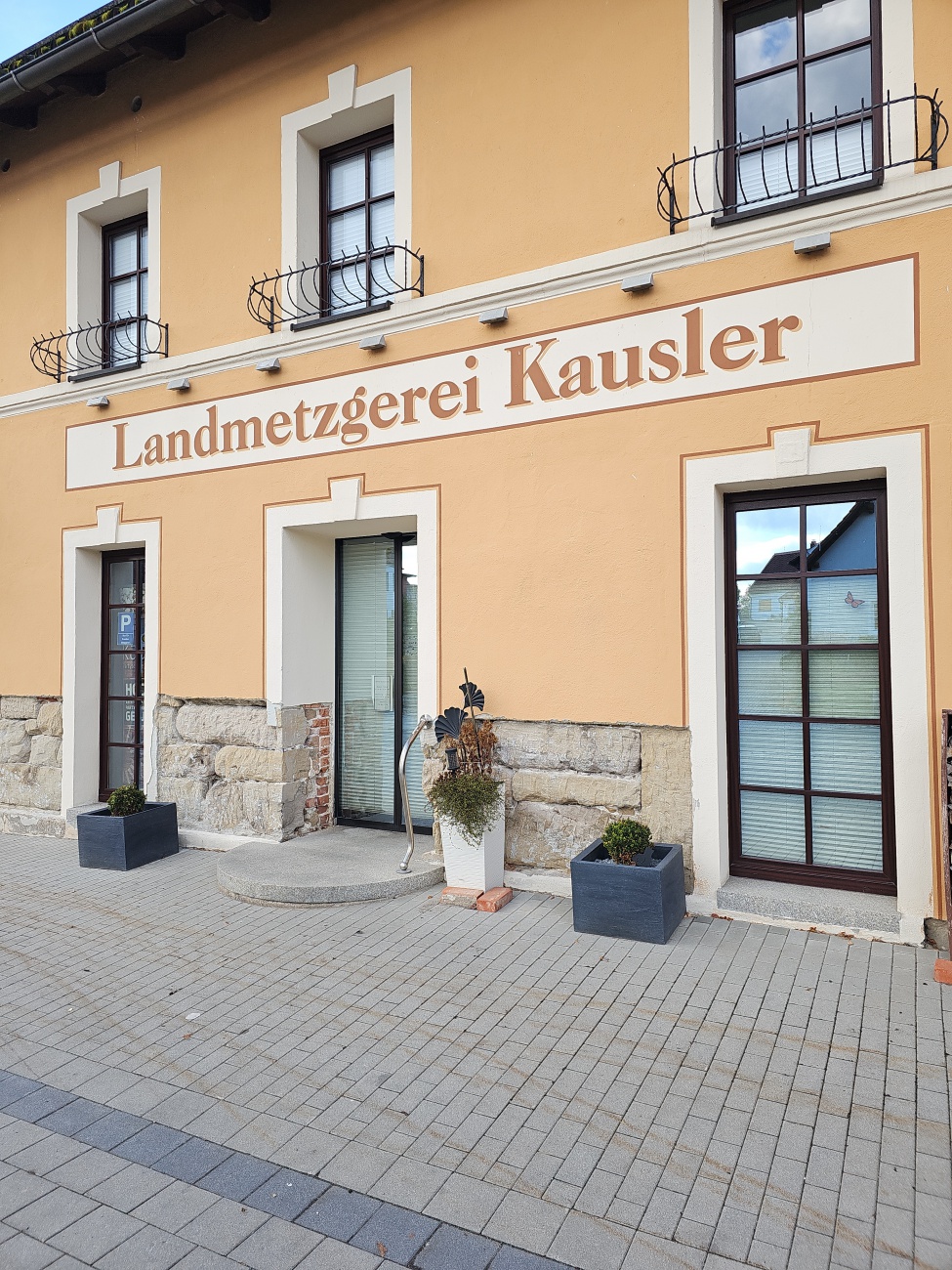 Warme Ockertöne und Naturstein betonen den gepflegten, traditionellen Charme der Landmetzgerei Kausler, die Handwerkskunst, Regionalität und Vertrauen ausstrahlt.