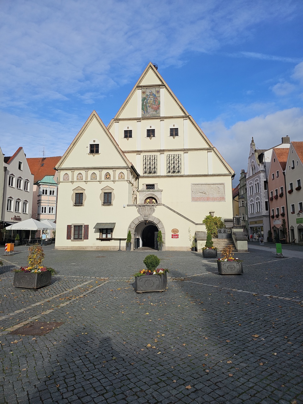 Das eindrucksvolle Giebelhaus mit kunstvollen Fassadenmalereien am Marktplatz in Weiden fällt mit seinem auffälligen Dreiecksgiebel sofort ins Auge. 

Als ehemaliges Rathaus war es lange das Zentrum des städtischen Lebens. Das große Wandgemälde verweist auf die historische Bedeutung des Gebäudes. Im Vordergrund setzen dezente Blumenkübel farbige Akzente und verleihen dem Platz eine lebendige Atmosphäre.