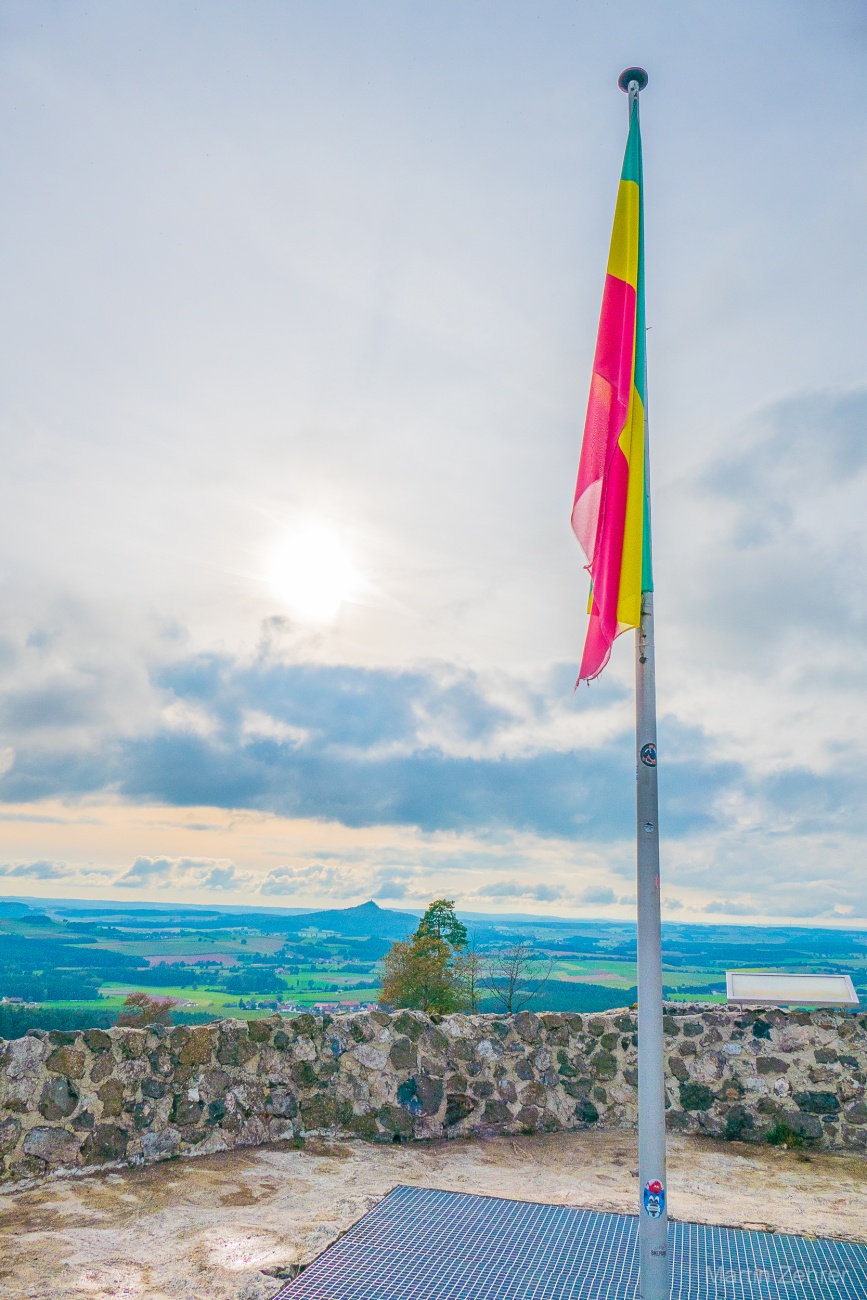 Foto: Martin Zehrer - Eine Fahne auf dem Schlossberg... Im Hintergrund die Sonne und der Vulkankegel  Rauher Kulm... 