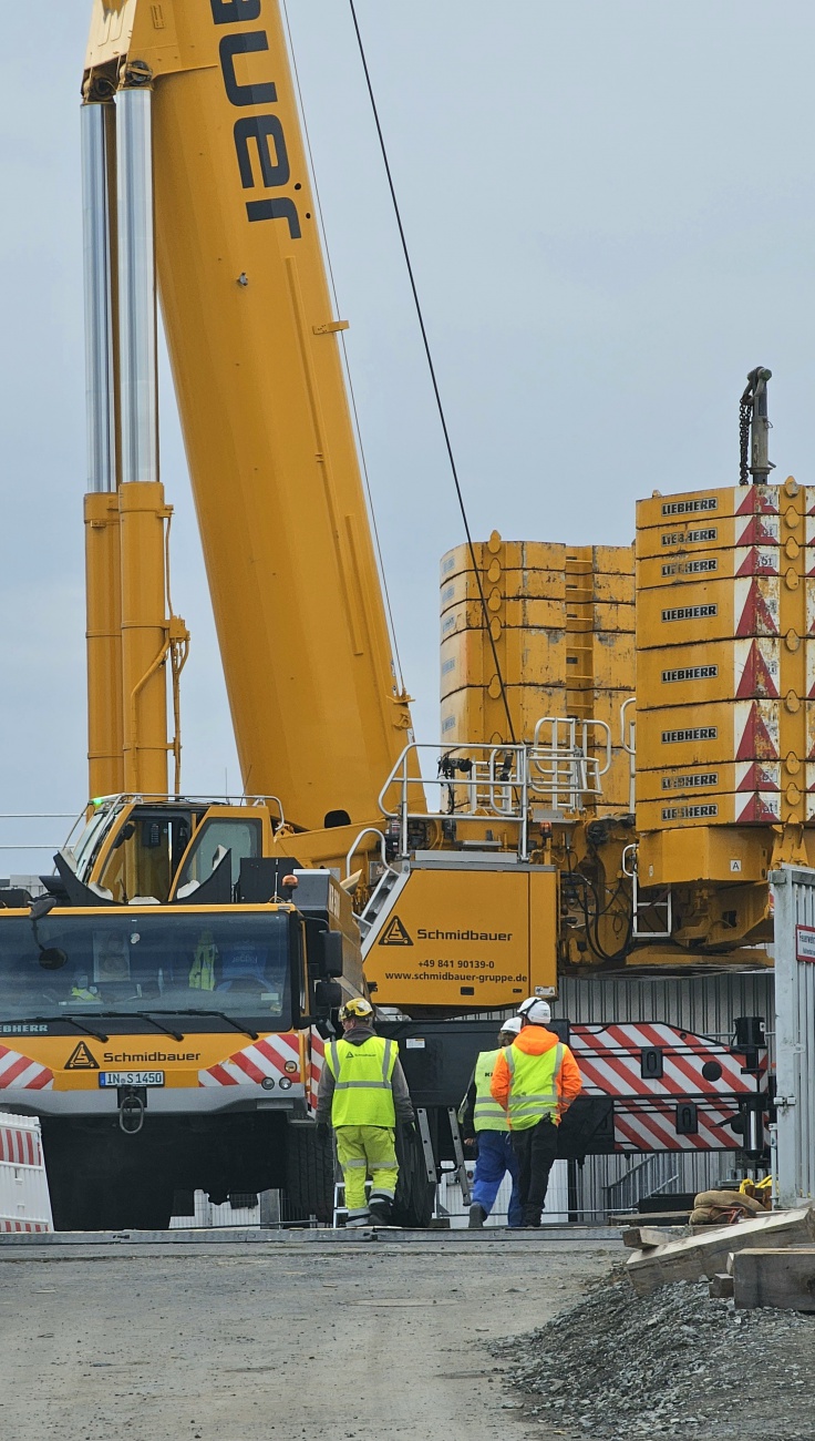 Schwerer Kraneinsatz auf der Siemens-Baustelle in Kemnath

Auf der Baustelle von Siemens Healthineers in Kemnath ist schweres Gerät im Einsatz. Ein mächtiger Liebherr-Mobilkran der Firma Schmidbauer steht mit zahlreichen Gegengewichten bereit. Mitarbeiter besprechen vor Ort die anstehenden Arbeiten.

Siemens Healthineers investiert rund 70 Millionen Euro in eine neue Montage- und Fertigungshalle für moderne Medizintechnik. Das Gebäude mit einer Fläche von rund 4.500 Quadratmetern soll künftig unter anderem der Fertigung von Komponenten für die Strahlentherapie dienen.

Die Inbetriebnahme ist für Mitte 2027 geplant. Mit der Erweiterung stärkt Siemens Healthineers seinen Standort Kemnath und sichert langfristig Arbeitsplätze in der Region.