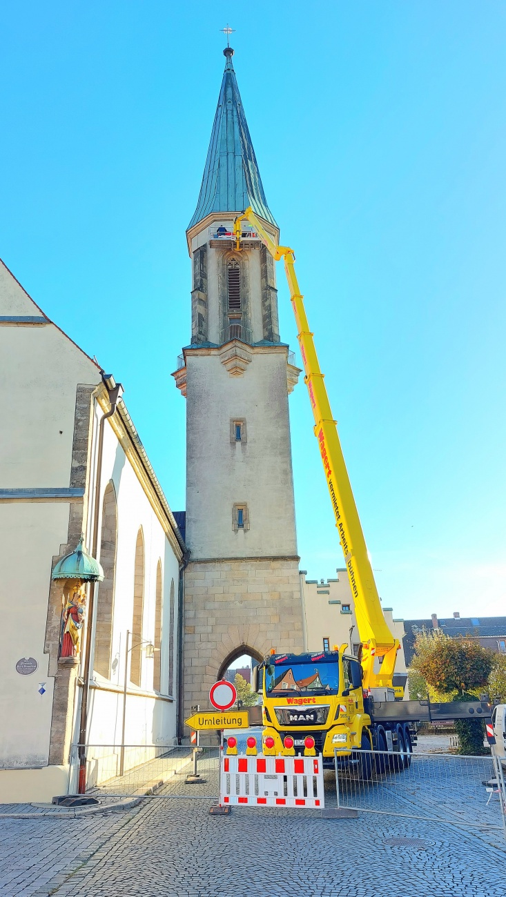 Foto: Martin Zehrer - Mit einem großen Kran werden die frisch restaurierten, mit Blattgold verzierten Zifferblätter wieder am Kirchturm montiert. In der Sonne leuchten die neuen Ziffern und ve 